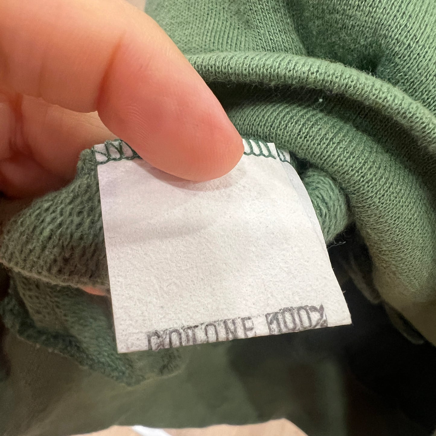 Close-up of a green sweater with a label held by a hand