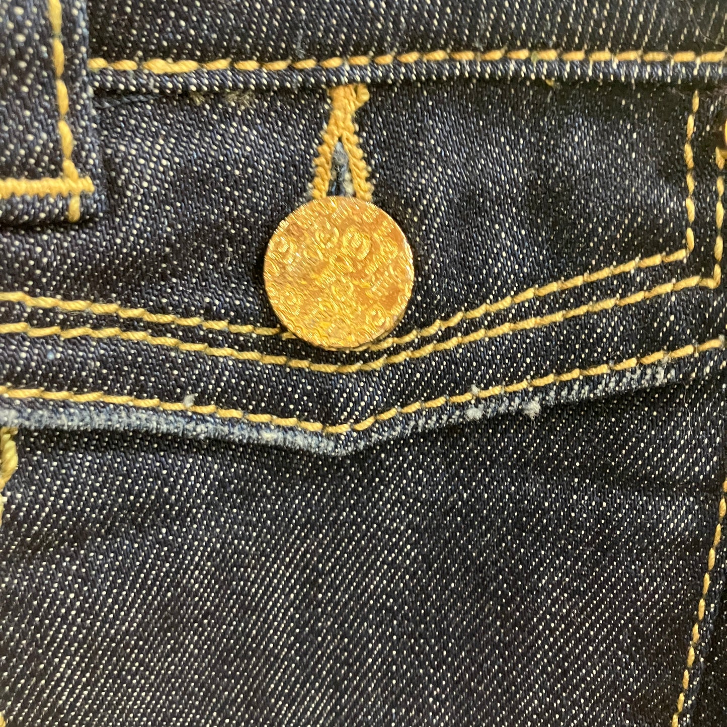 Close-up of a gold button on a black denim fabric
