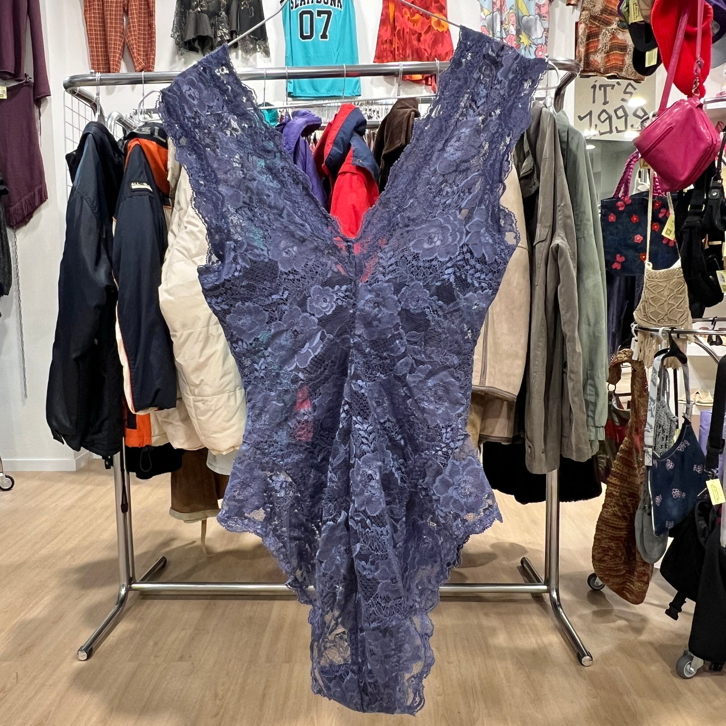 Blue lace dress hanging on a rack in a store with various clothing items in the background