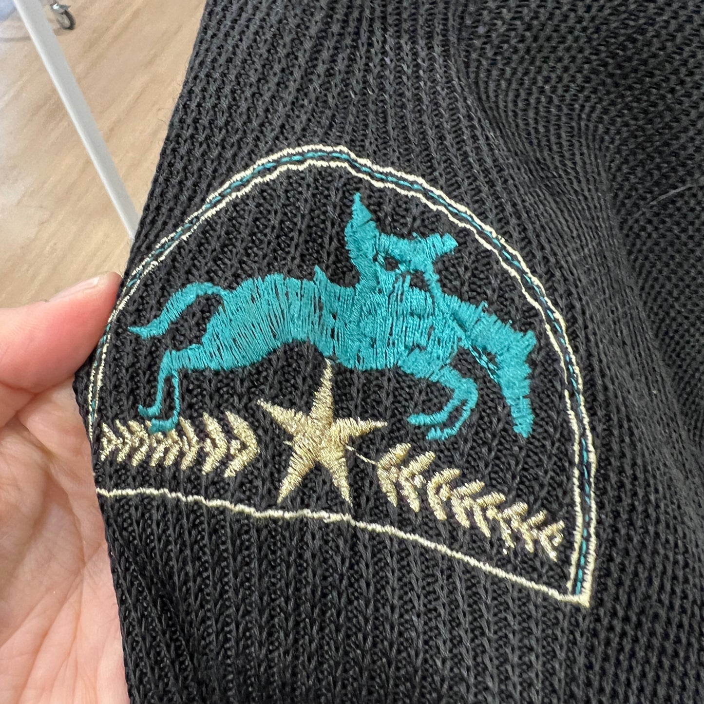 Black sock with teal and gold embroidered design held by a hand