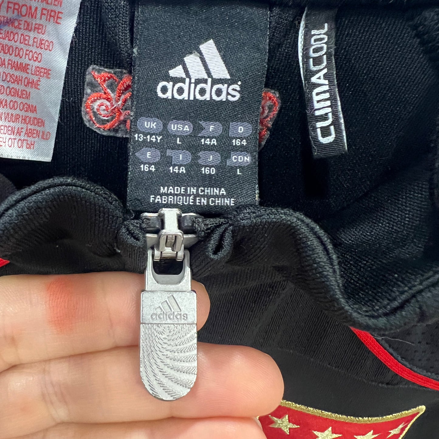 Close-up of Adidas shoe with label and zipper held by a hand