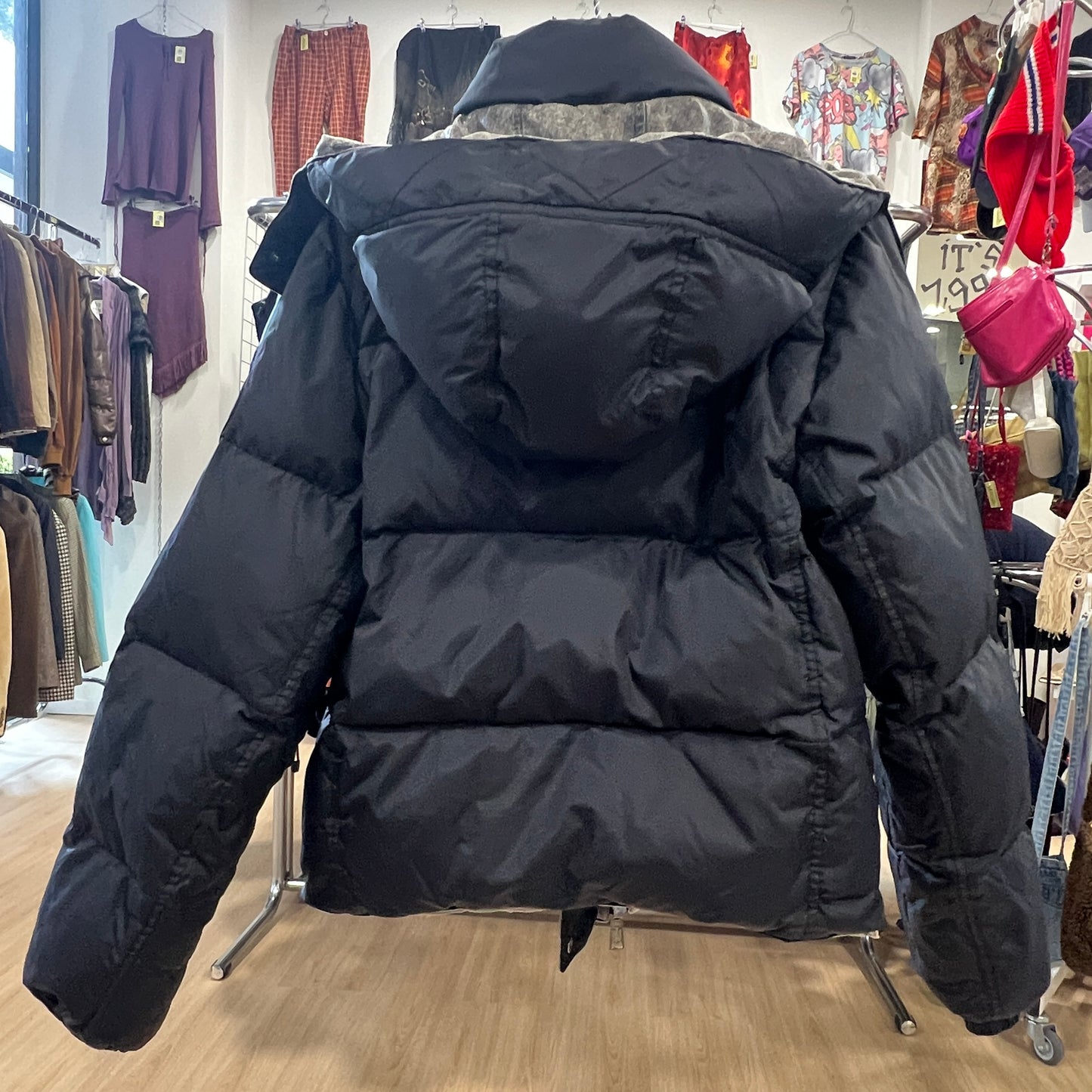 Black puffer jacket in a store setting with various clothing items in the background