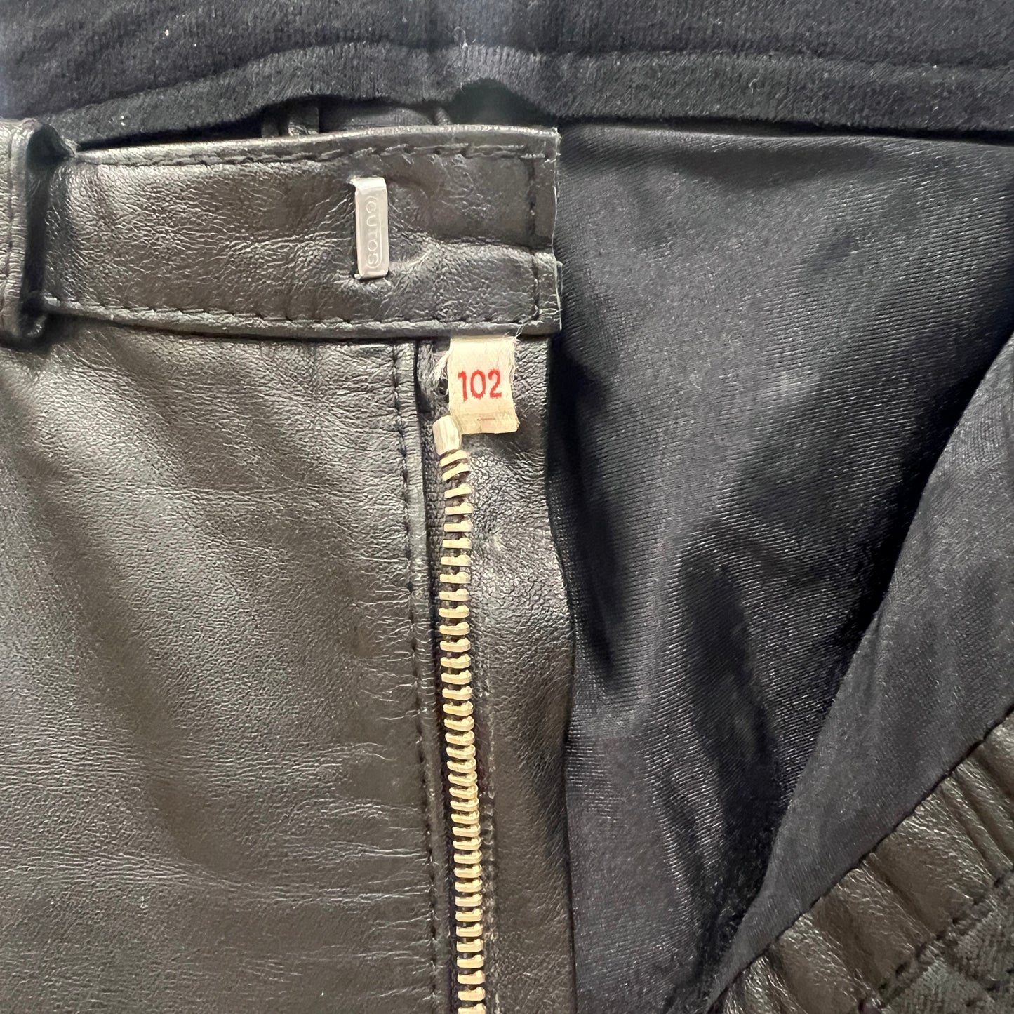 Close-up of a black leather pants with a zipper and visible brand label