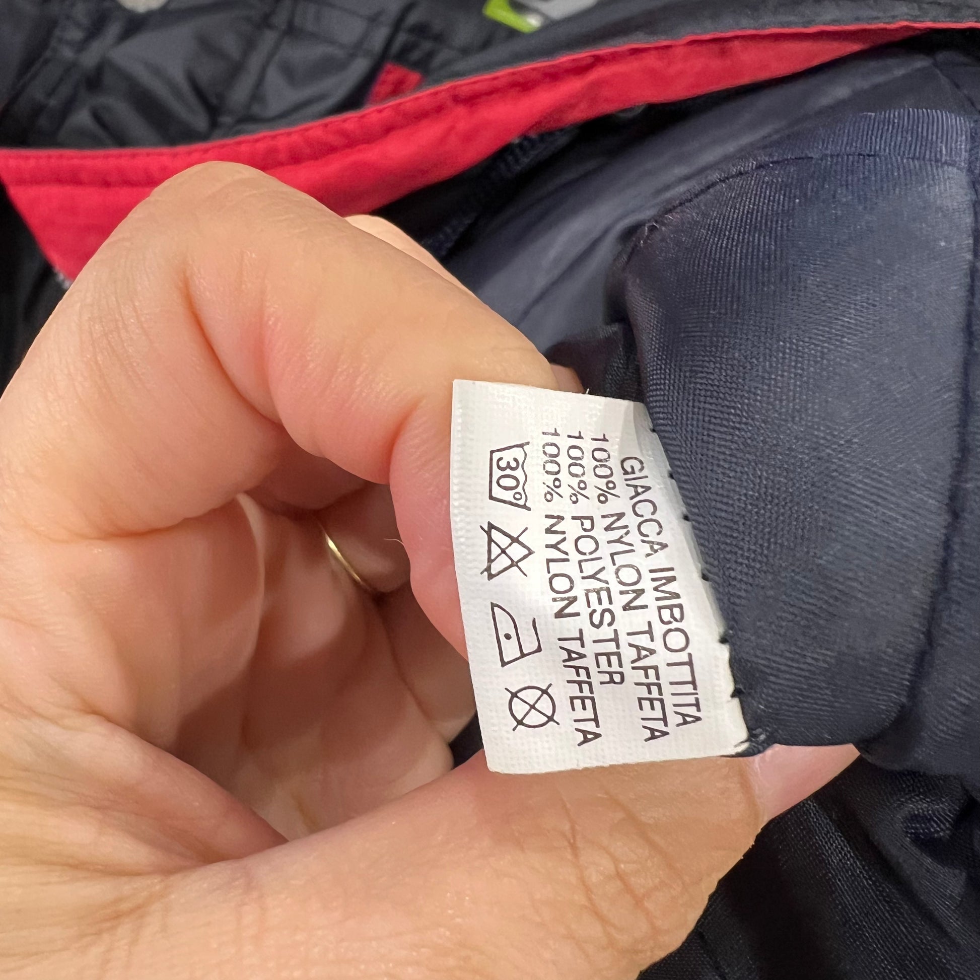 Hand holding a clothing label on a jacket with visible text and symbols