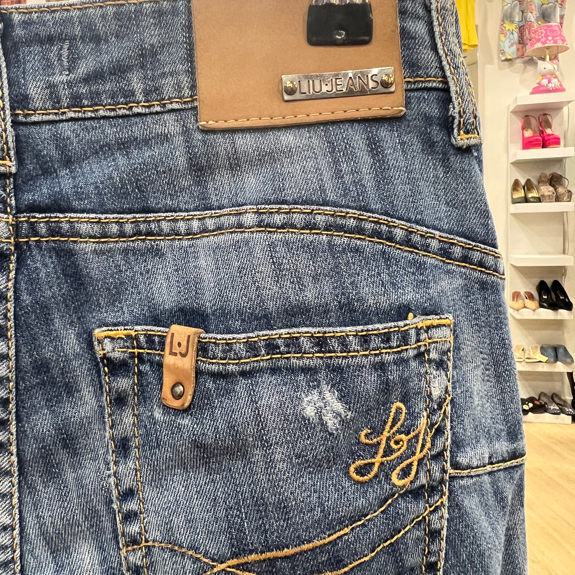 Close-up of blue jeans with a brand label and 'liu jeans' embroidery in a store setting