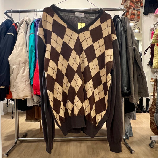 Checkered sweater on a clothing rack with various other garments in a store setting