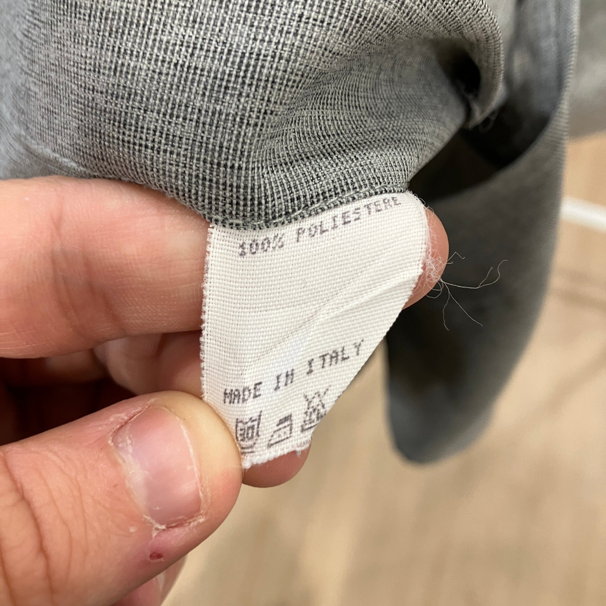 Hand holding a clothing label with text and symbols on a blurred background