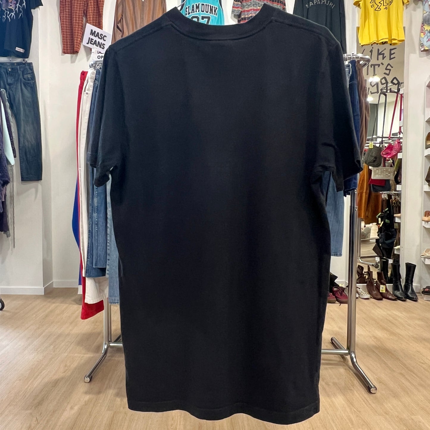 Black t-shirt on a hanger in a clothing store with various items in the background