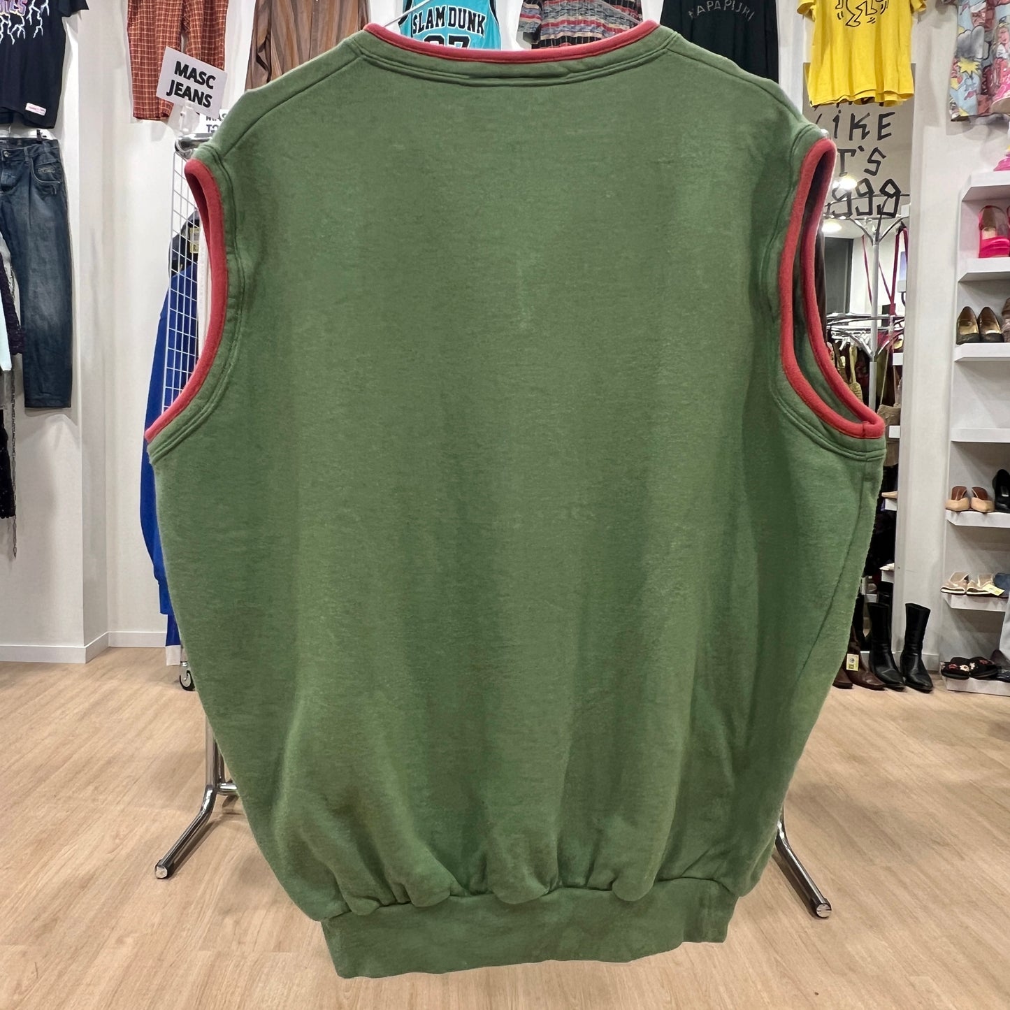 Green sleeveless top with red trim on a hanger in a store setting