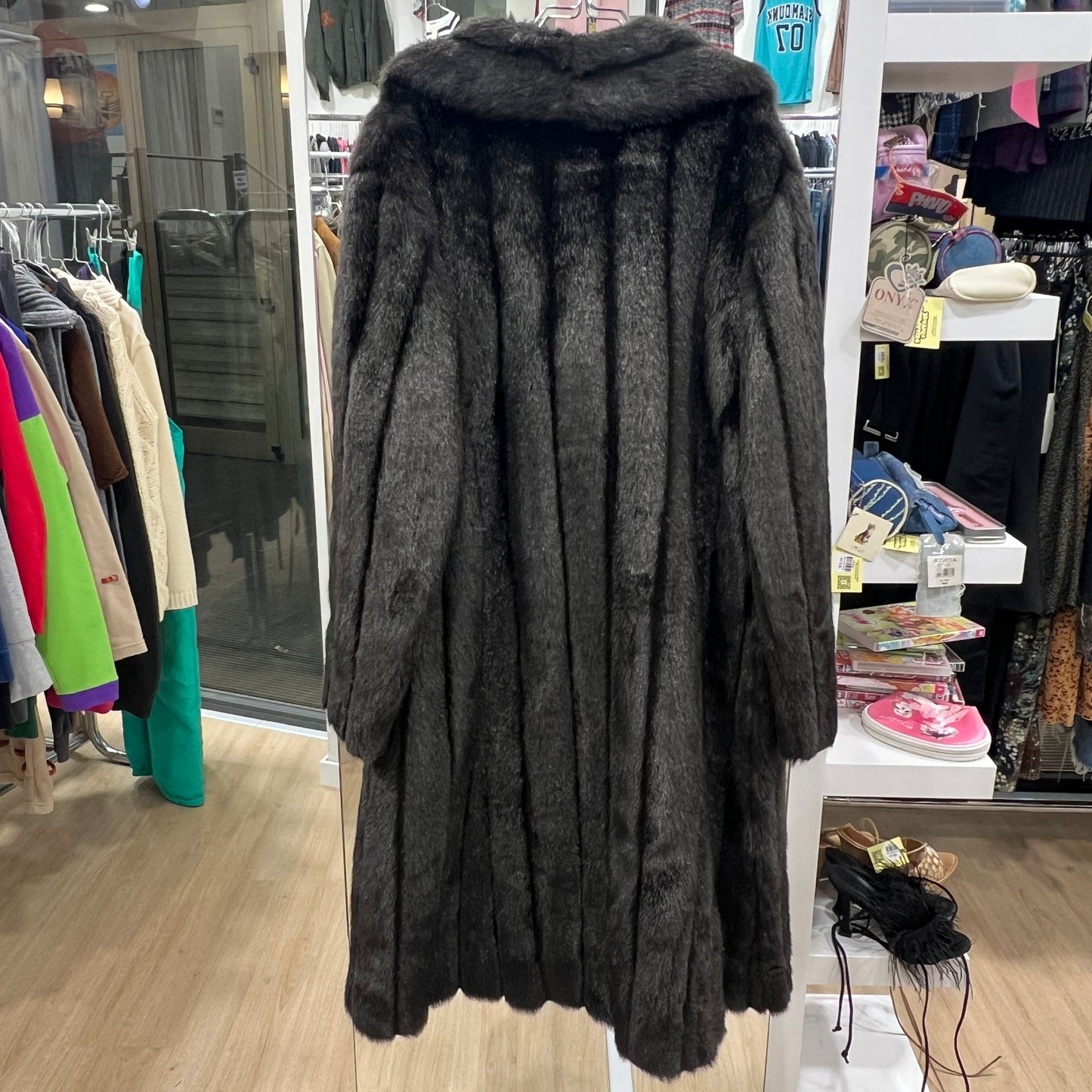 Dark brown fur coat displayed in a store setting with racks of clothes in the background