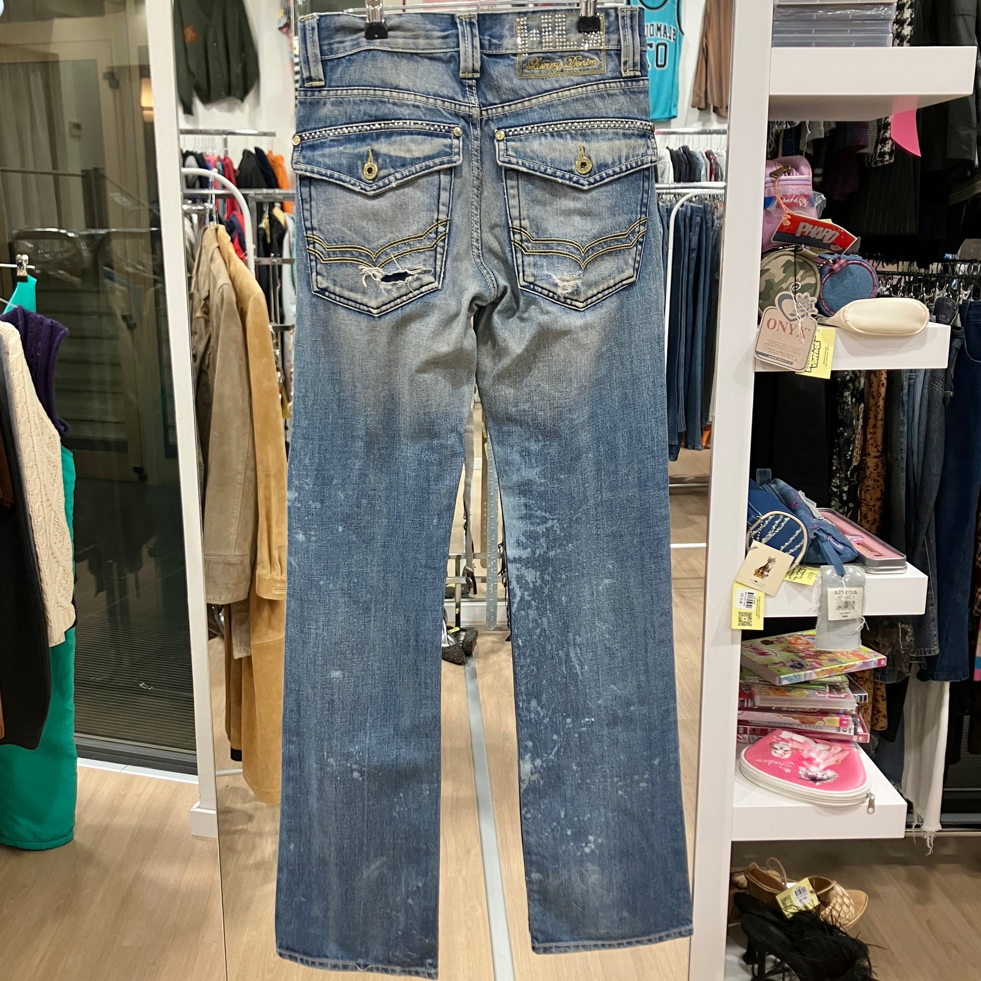 Blue jeans displayed on a rack in a store setting with various items and clothing in the background