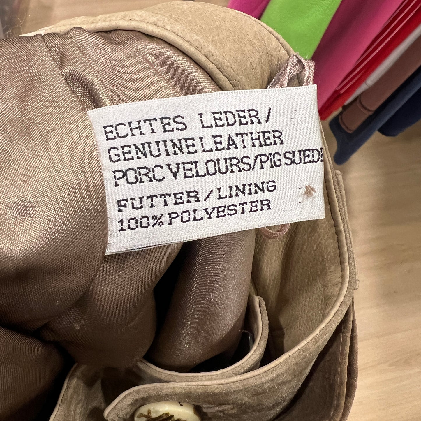 Close-up of a beige garment label showing ‘Genuine Leather’, ‘Pig Suede’, and ‘100% Polyester Lining’