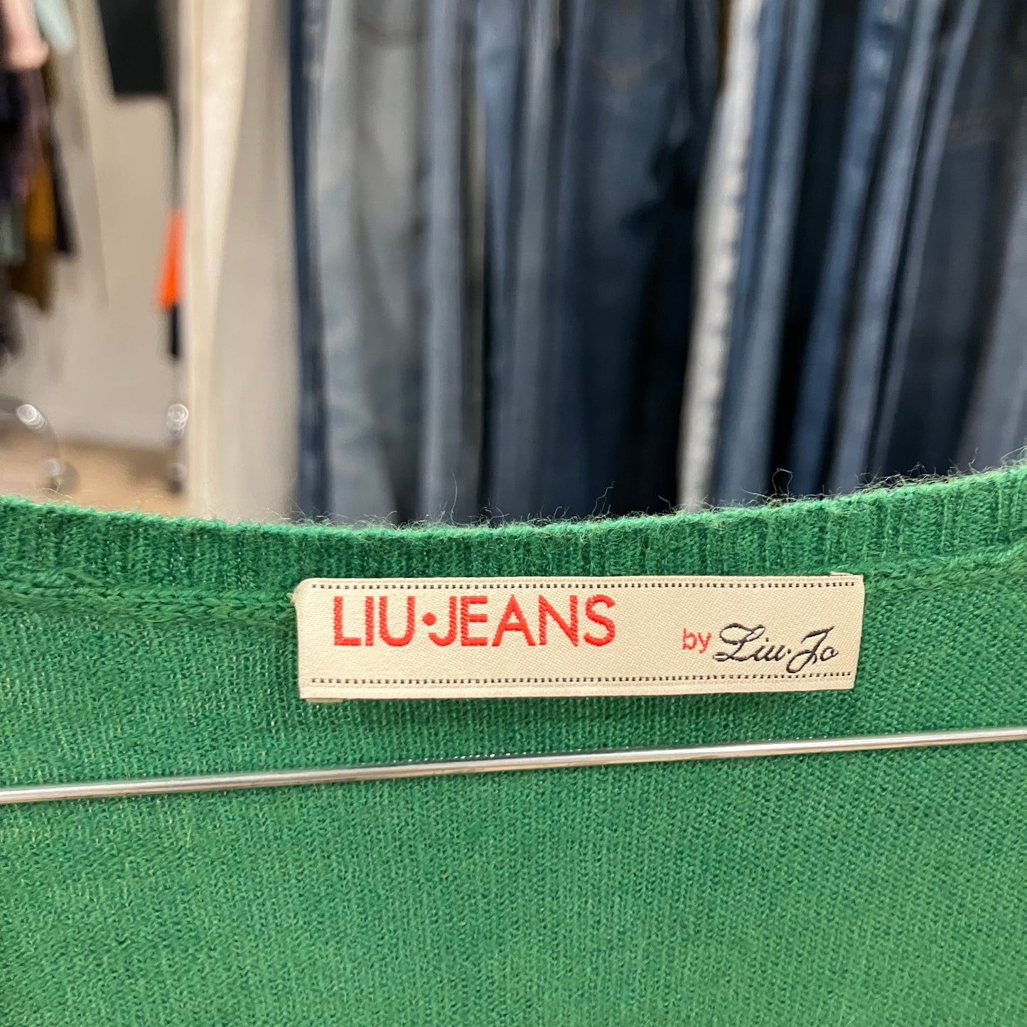 Green garment with a 'LIU JEANS by Liu Jo' label against a blurred clothing background
