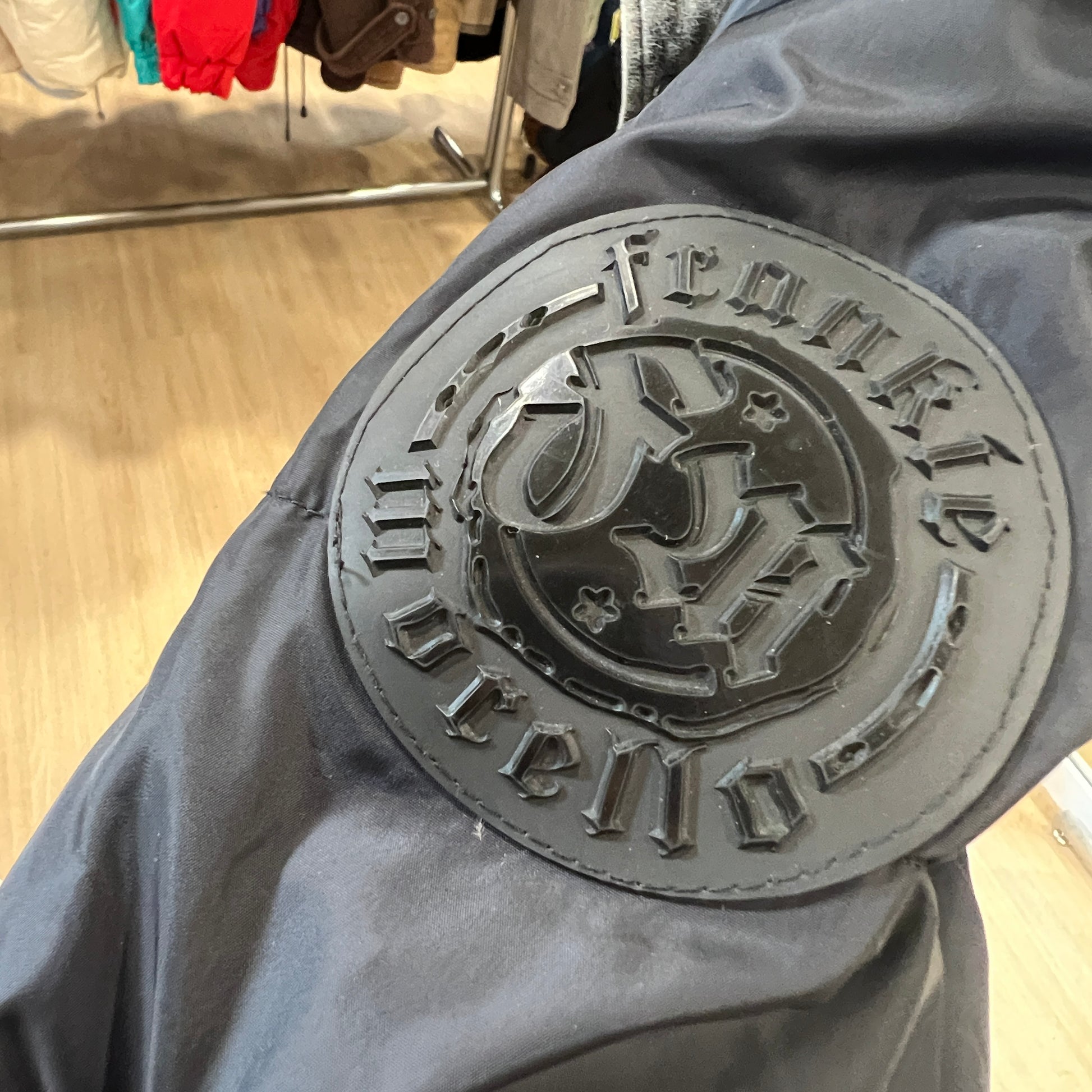 Close-up of a gray jacket with a brand logo patch on a clothing store floor