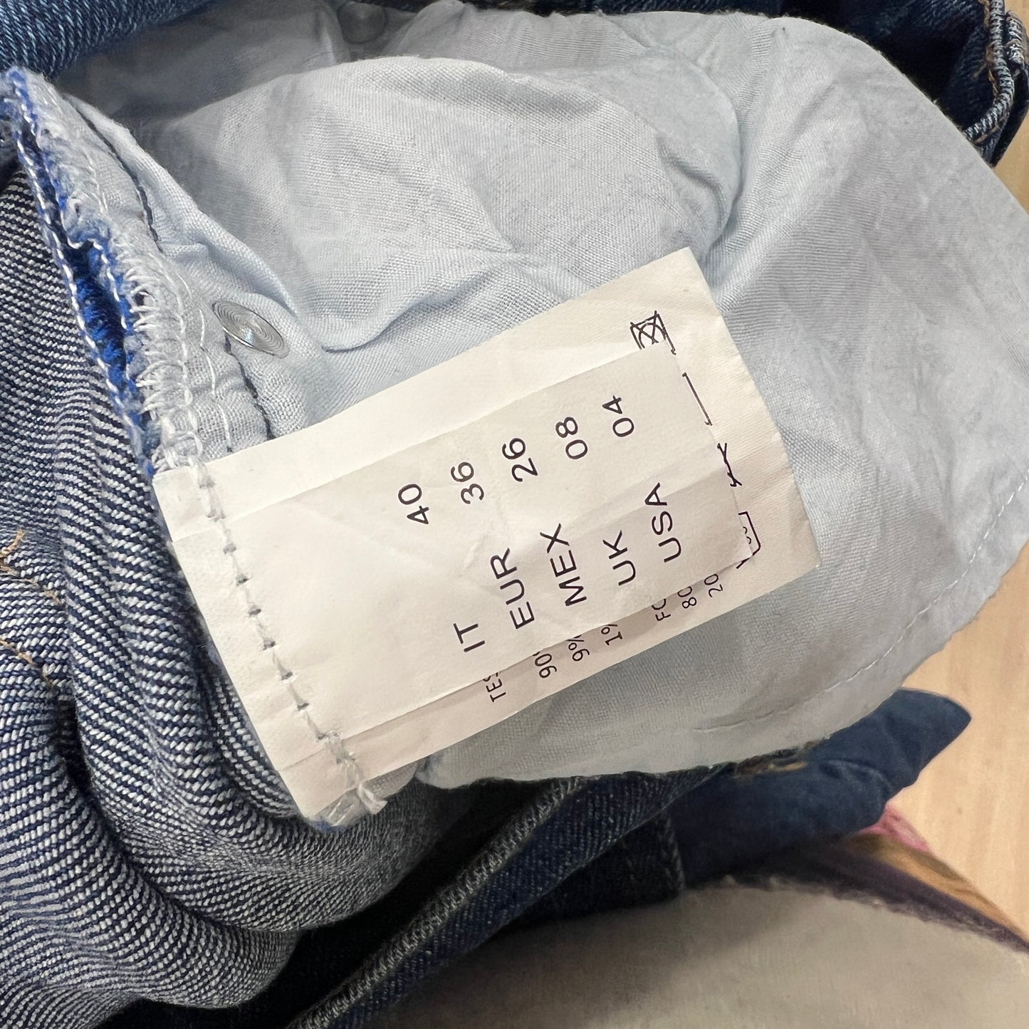 Close-up of a denim garment with a size label on a wooden surface
