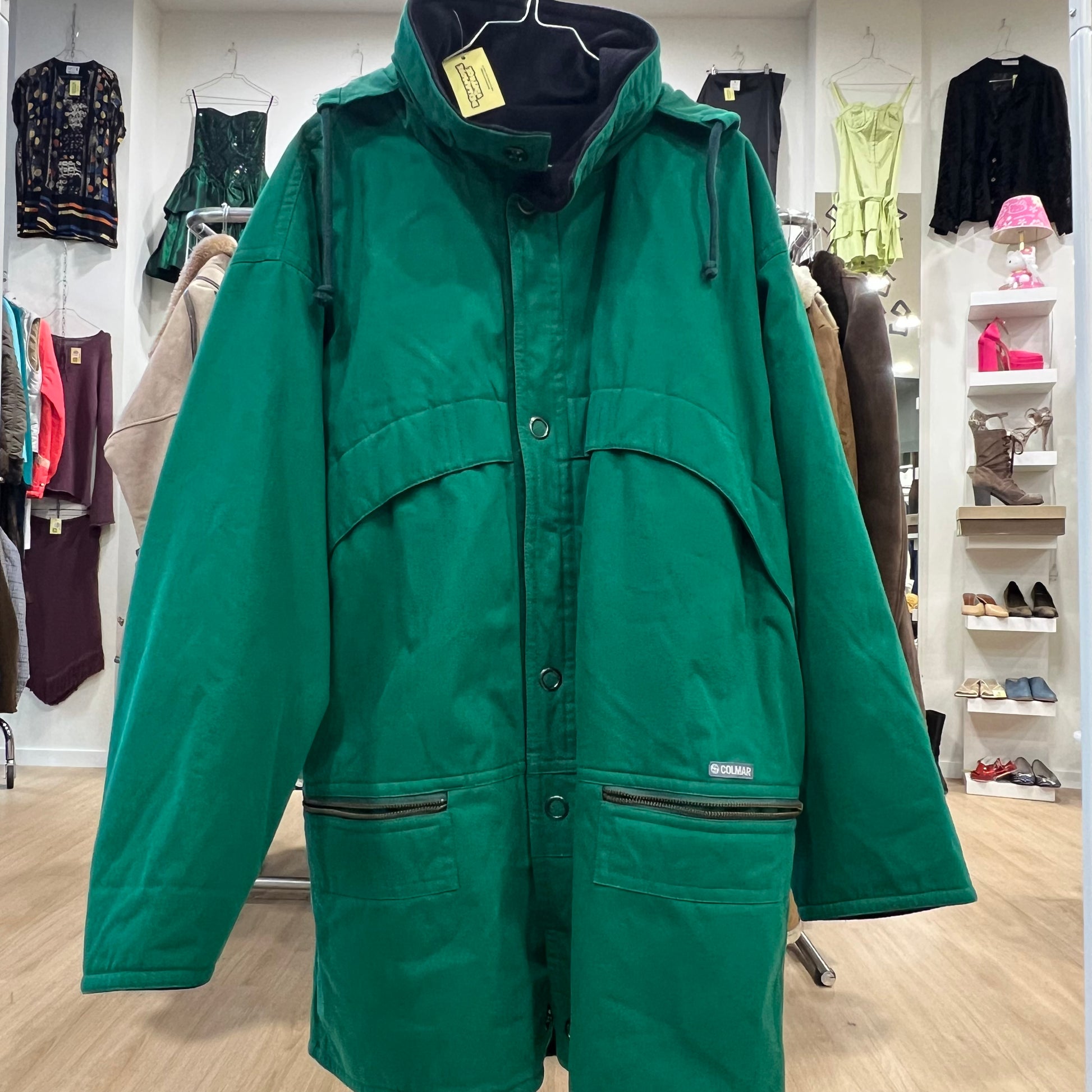 Green jacket on a hanger in a store setting with various clothing items in the background