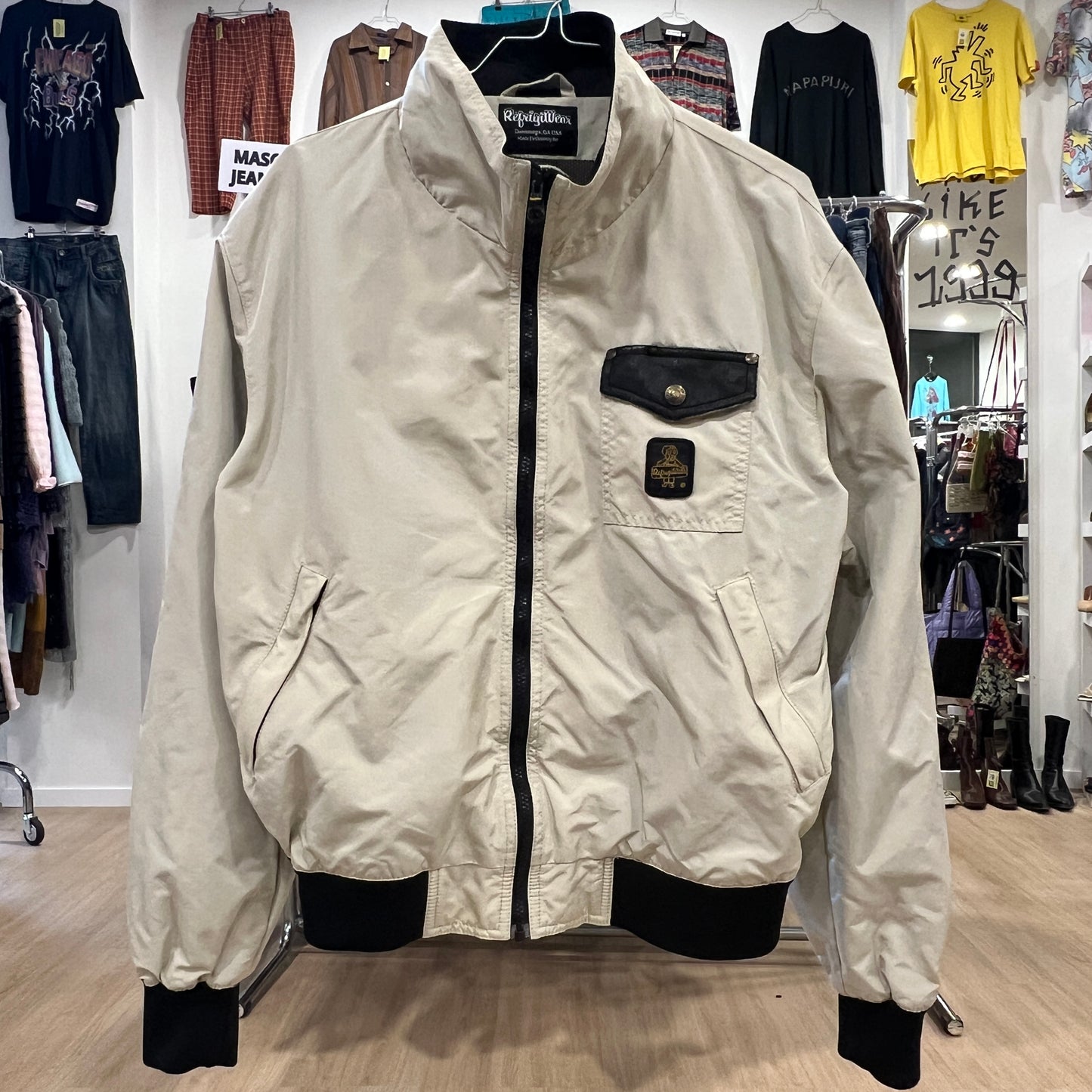 Front view of a beige vintage jacket with black zipper, black chest pocket, and ribbed cuffs and hem, displayed on a hanger ins
