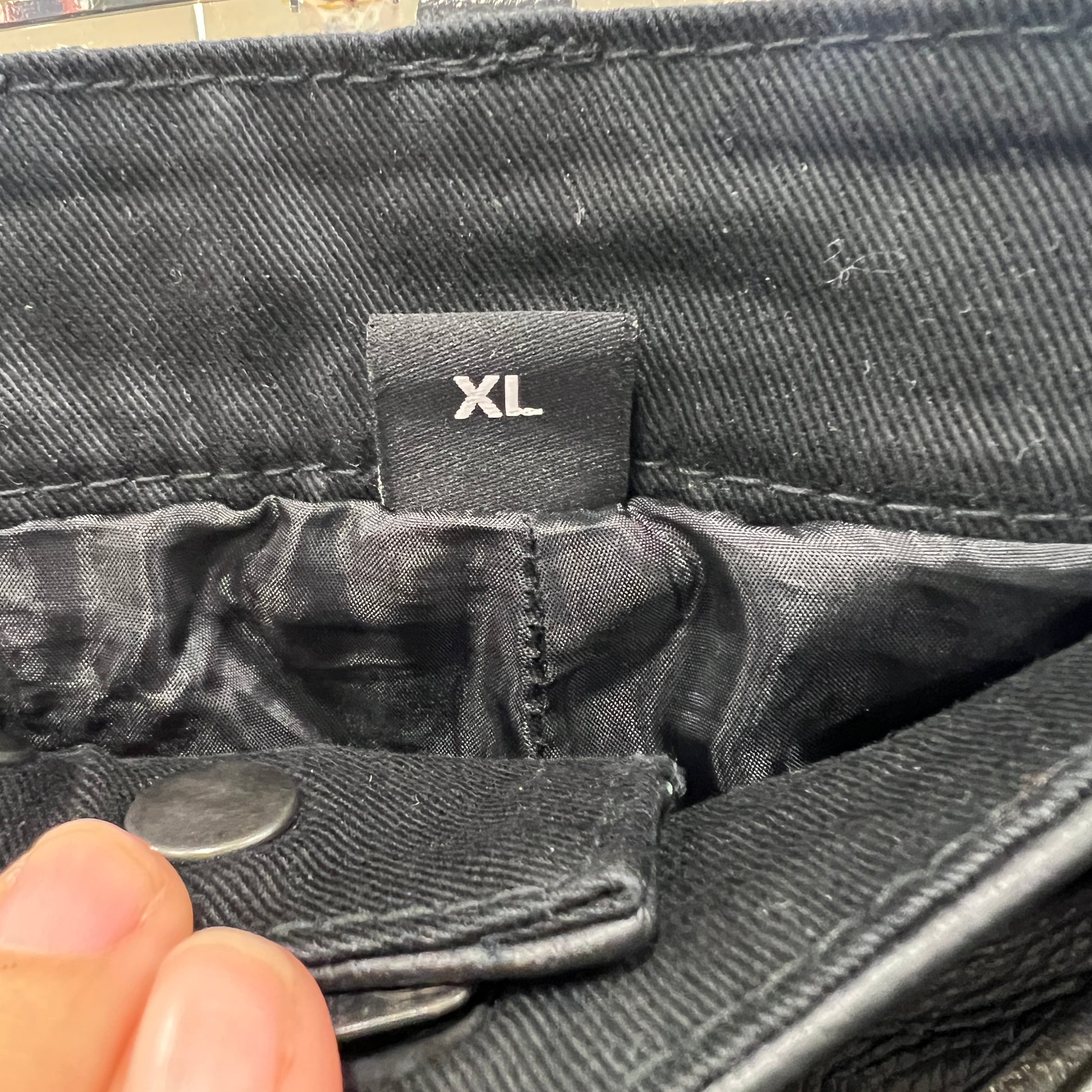 Close-up of a black leather pants pocket with an 'XL' tag