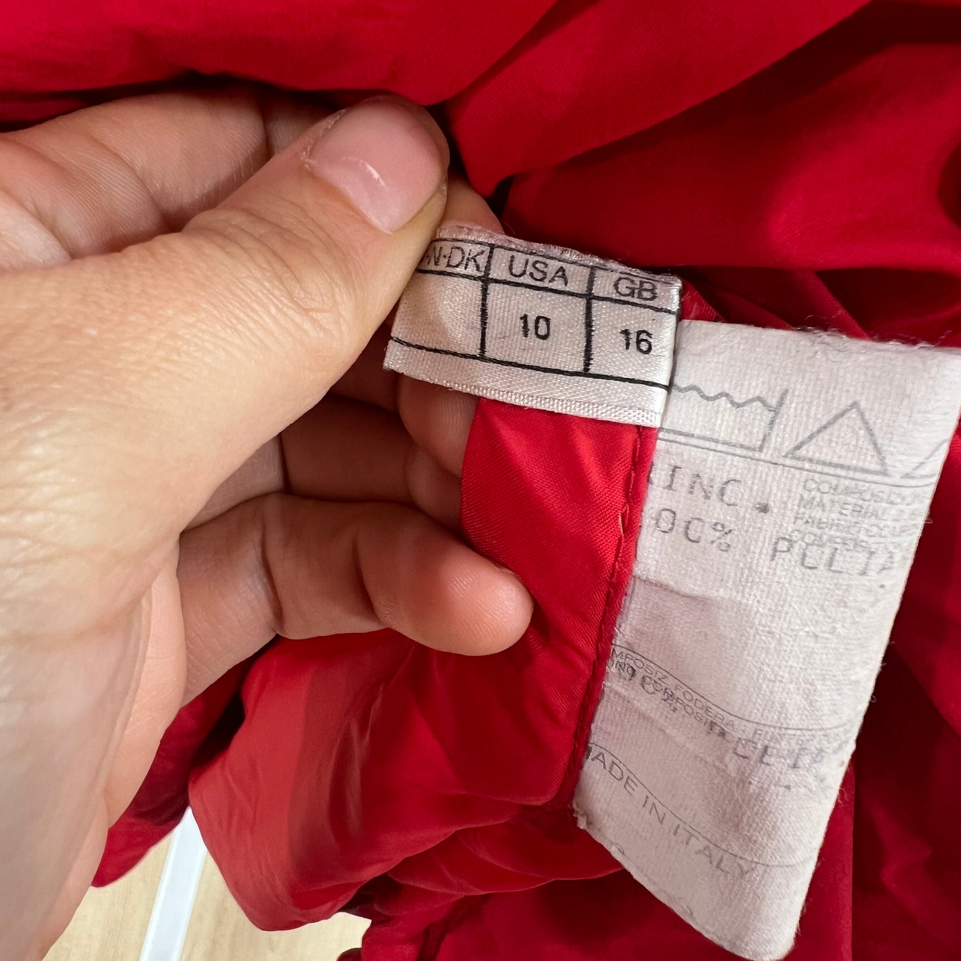 Close-up of a red garment with a size label held by a hand