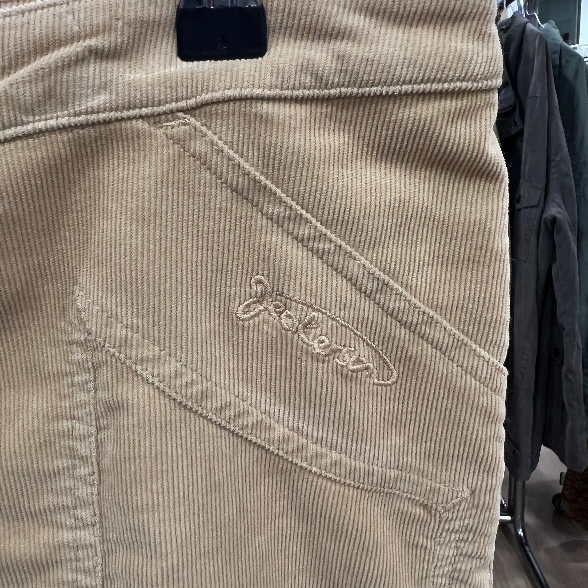 Beige corduroy pants with a brand logo on the pocket, hanging on a rack