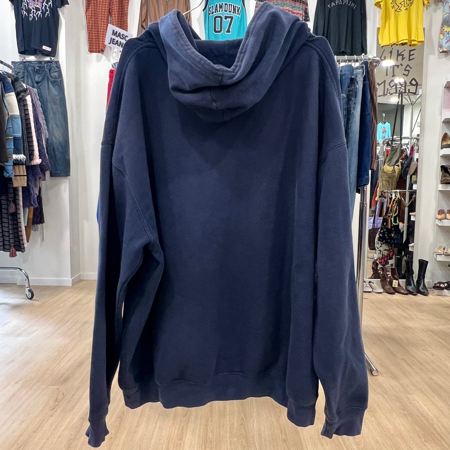 Navy blue hoodie displayed in a store with clothing racks in the background
