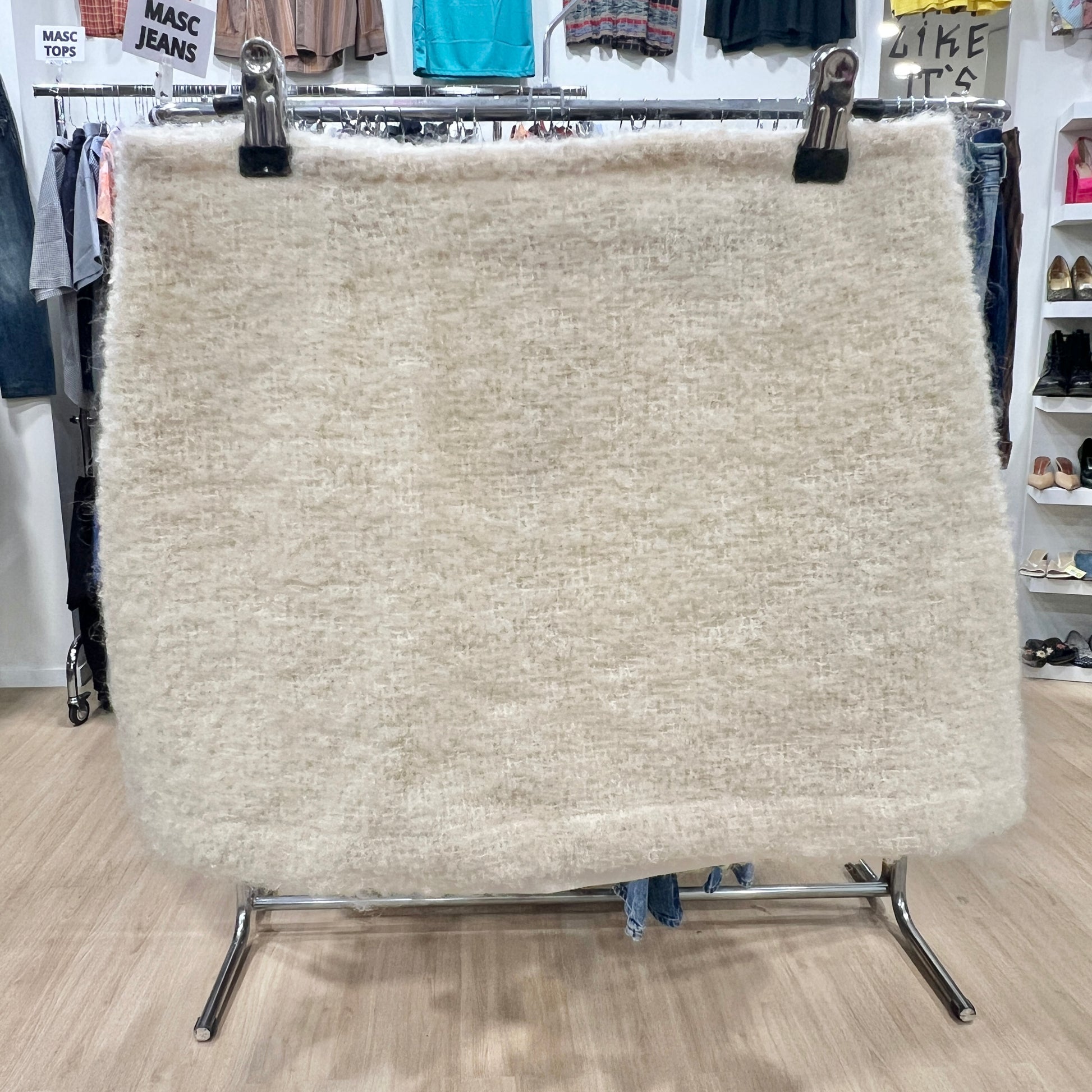 Textured fabric sample on a stand in a retail setting with clothing in the background