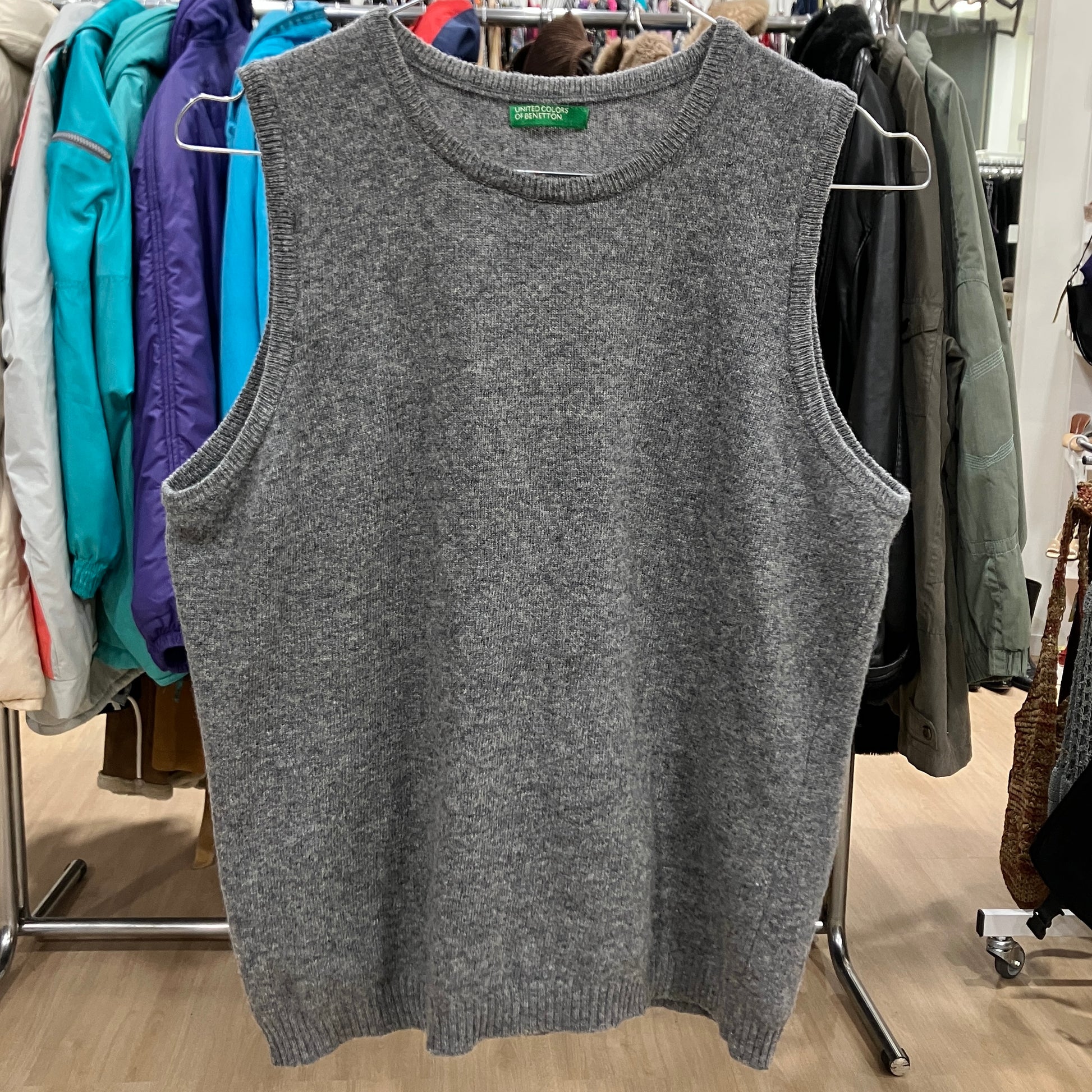 Gray sleeveless sweater vest on a hanger with a clothing rack in the background