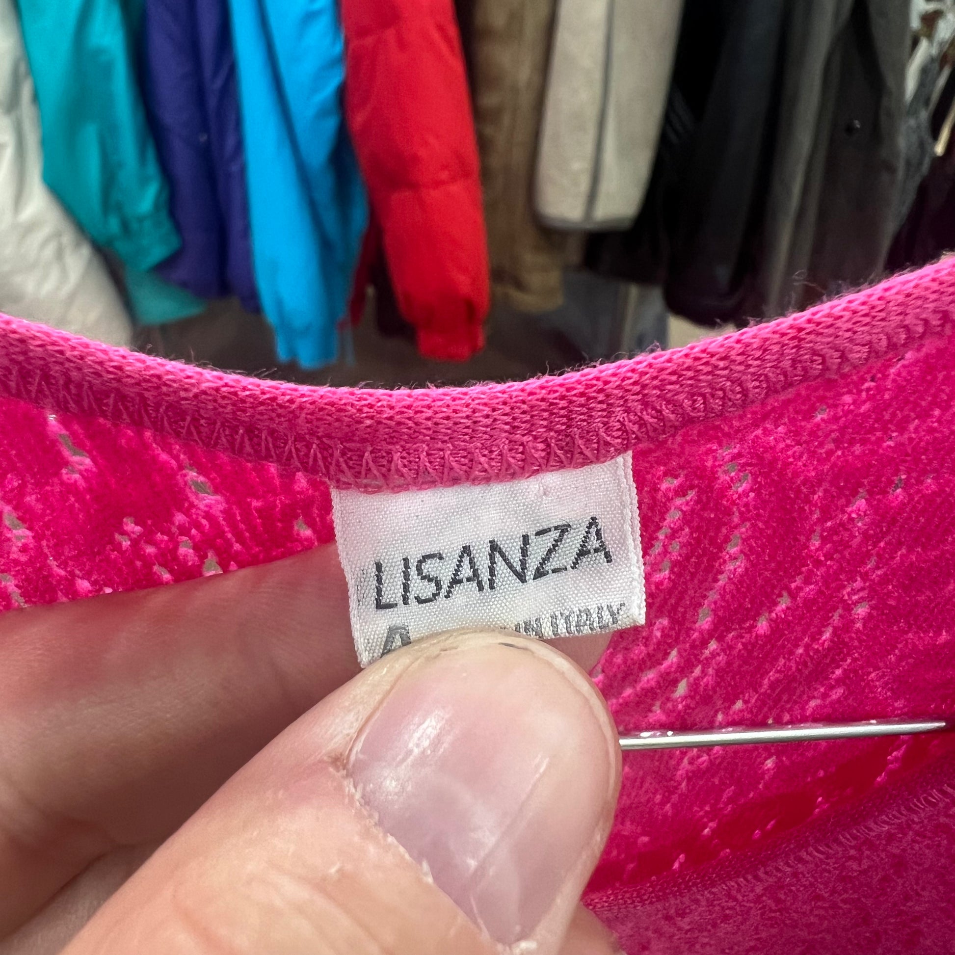Pink fabric with a 'Lisanza' label held by a hand against a background of clothes on a rack