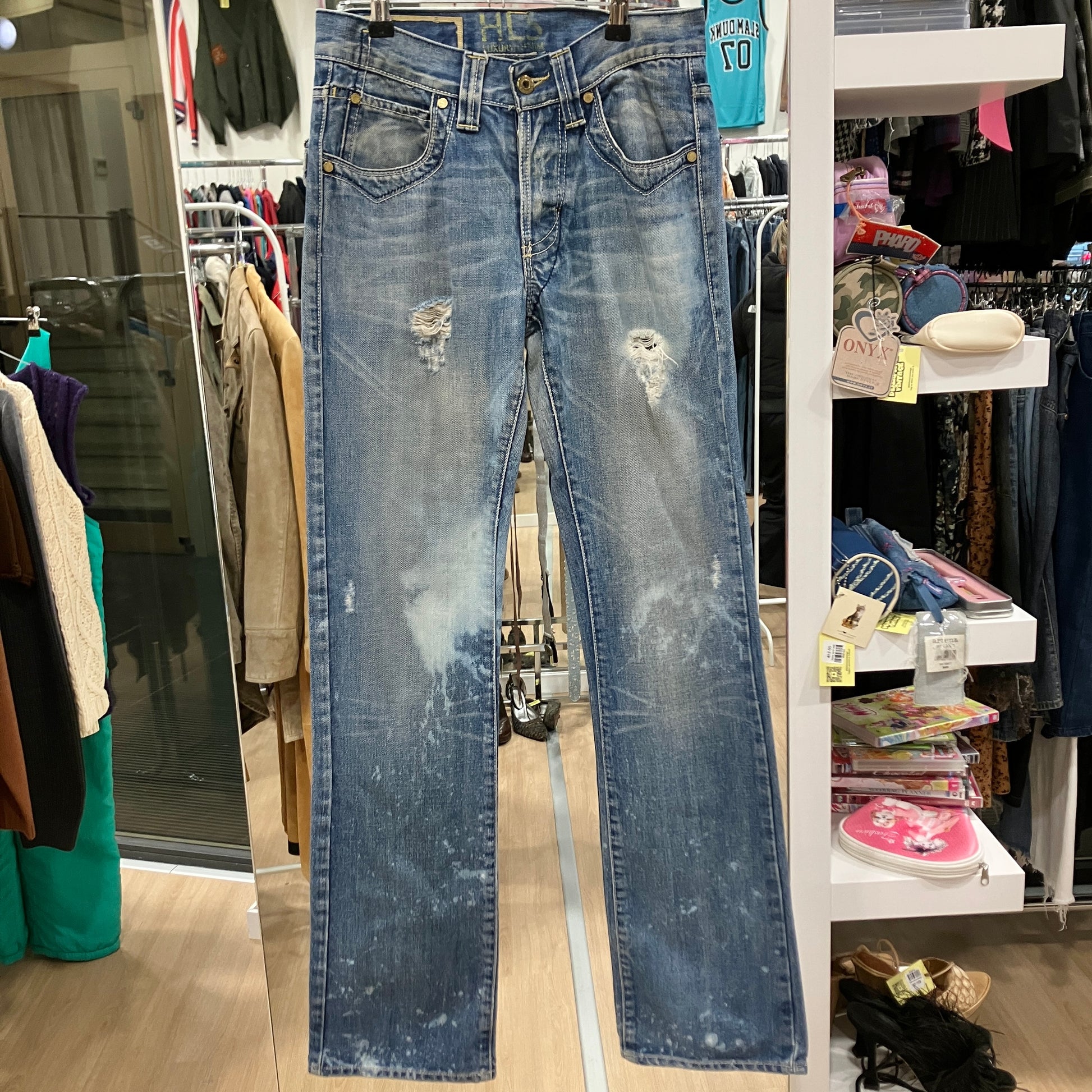 Distressed blue jeans hanging in a store setting with racks and shelves in the background