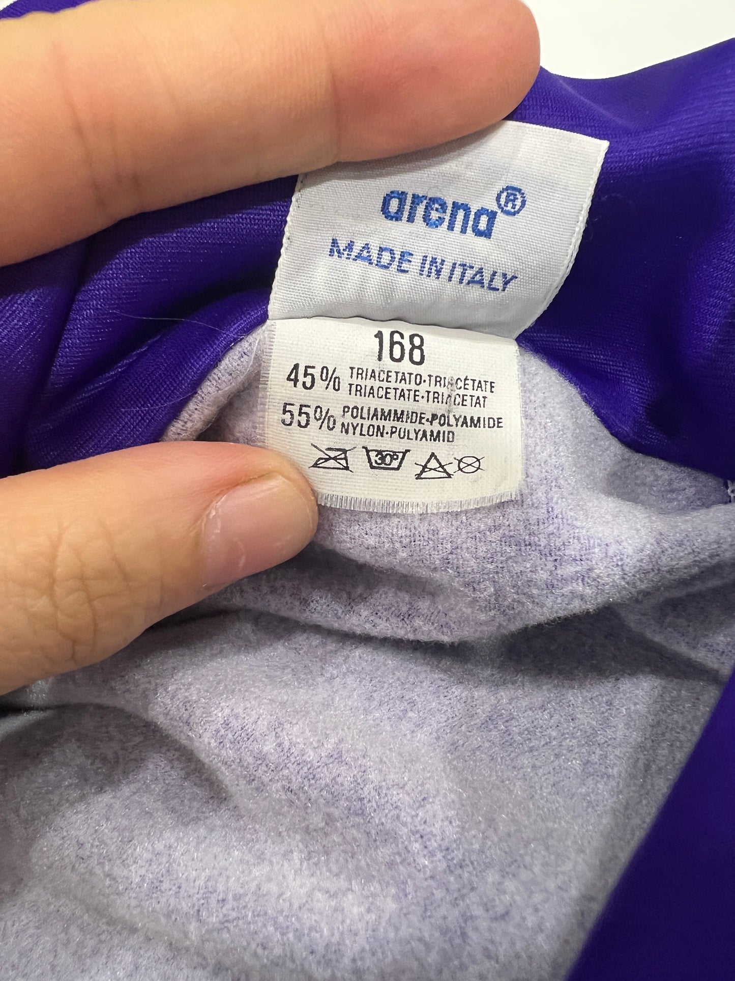 Close-up of a fabric tag with 'Arena' branding on a purple and gray garment