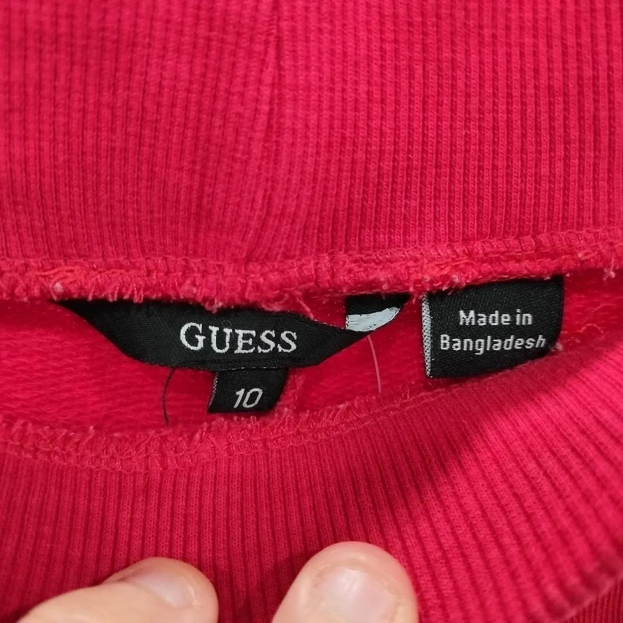 Close-up of red ribbed garment with tags showing size 10 and made in Bangladesh