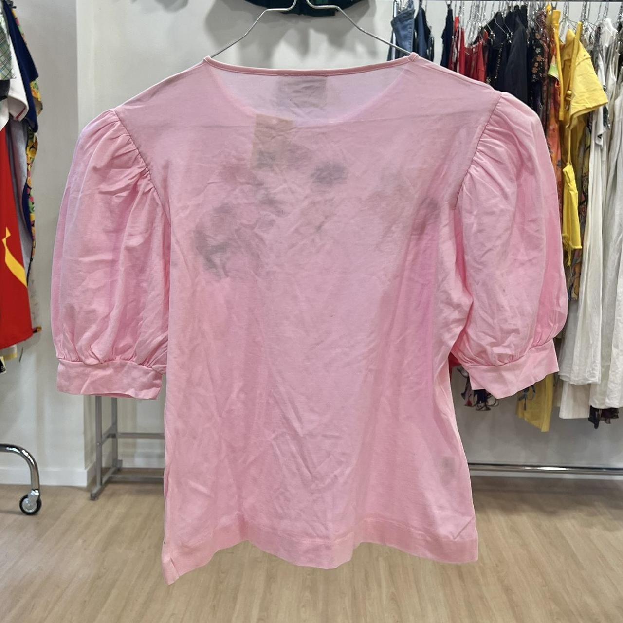 Pink blouse with sheer overlay on a hanger against a clothing store background