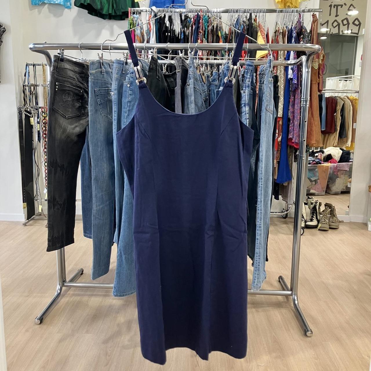 Navy blue dress hanging on a clothing rack with jeans and other garments in a store setting