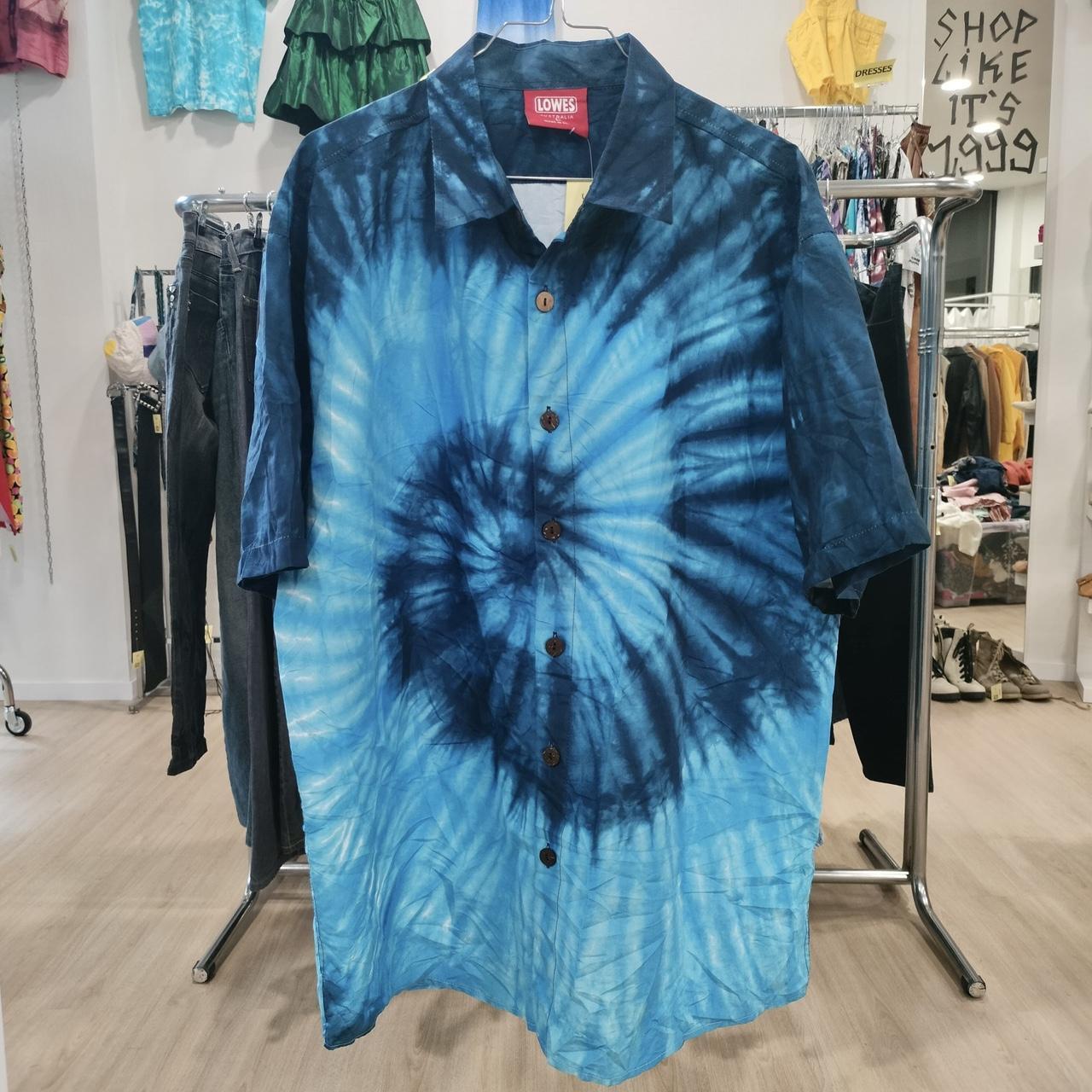 Blue tie-dye button-up shirt with short sleeves hanging in second hand clothing store