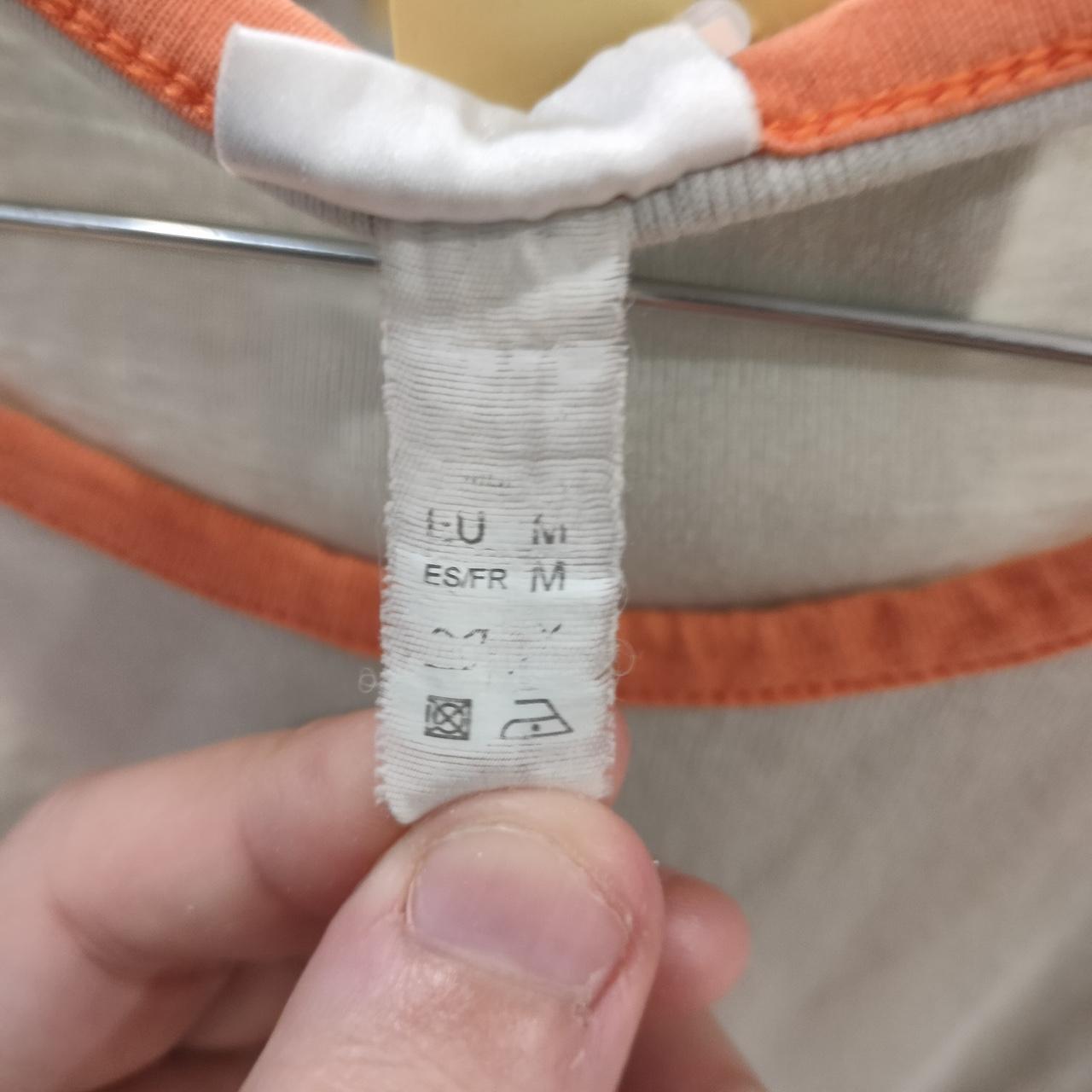 Close-up of clothing label with size medium tag on an orange-trimmed beige shirt