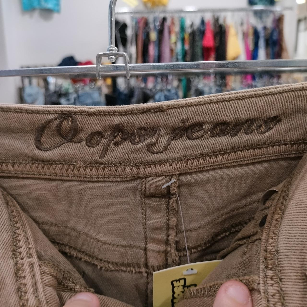 Close-up of brown second hand jeans with 'Oops jeans' label in a thrift store setting