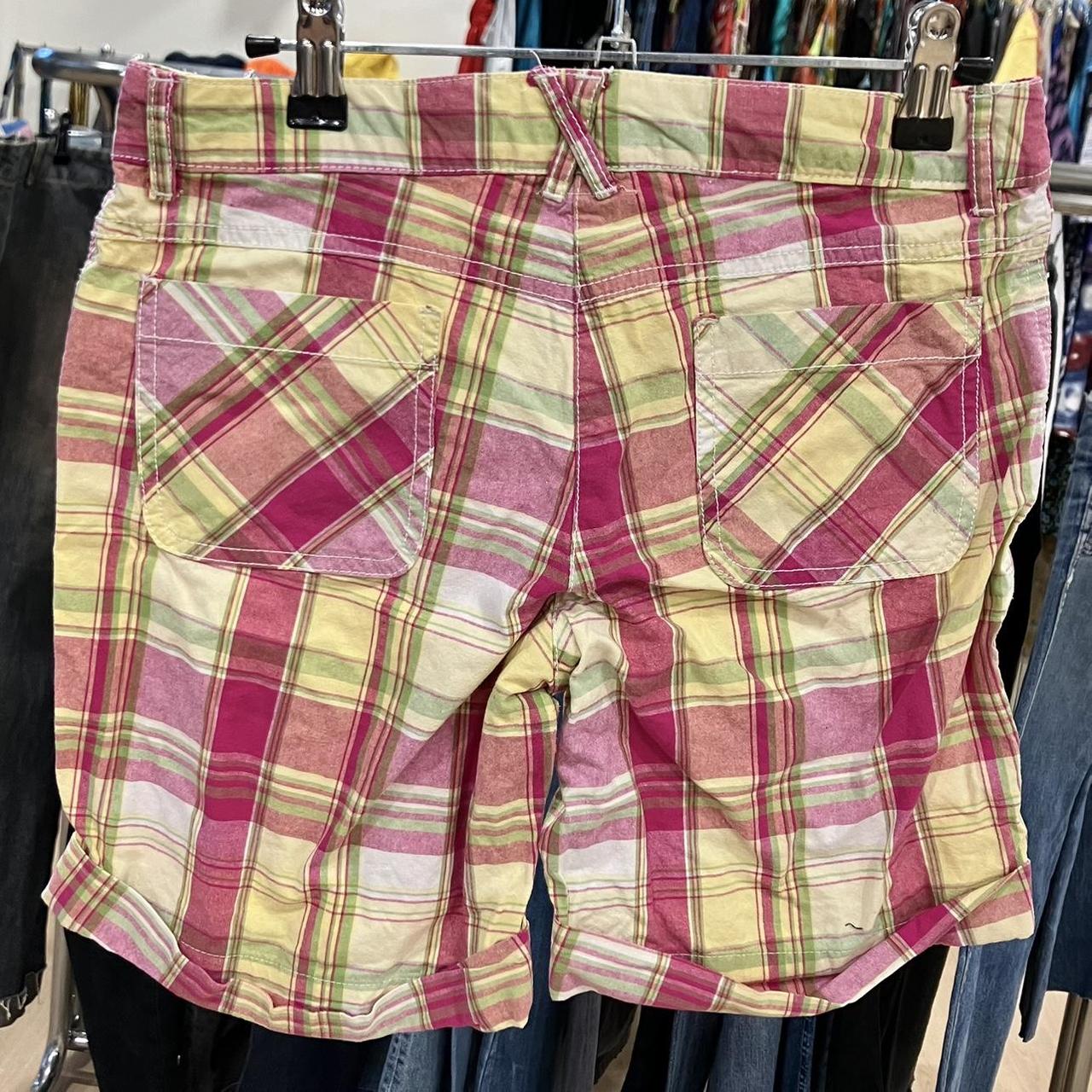 Colorful plaid shorts with back pockets in pink, yellow, and green, displayed on a rack