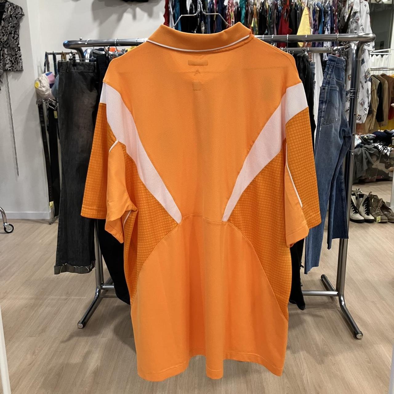 Orange polo shirt with white accents on a rack in a store setting