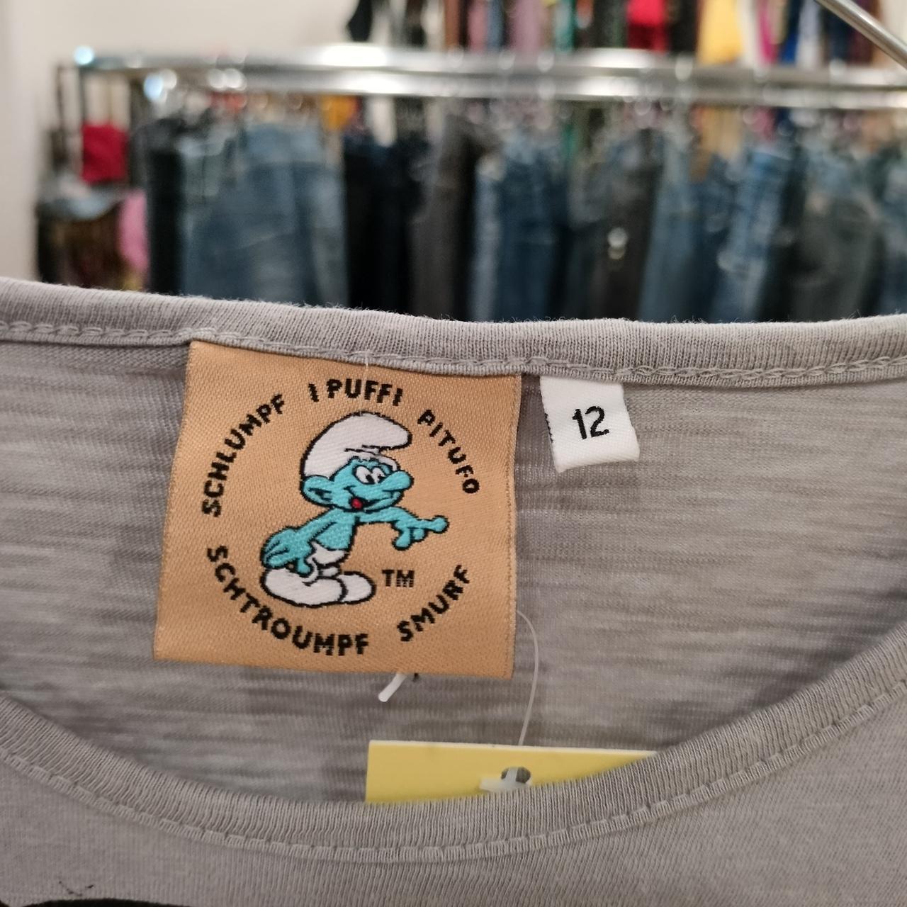 Close-up of a Smurf character tag on a gray t-shirt, sustainable fashion, size 12