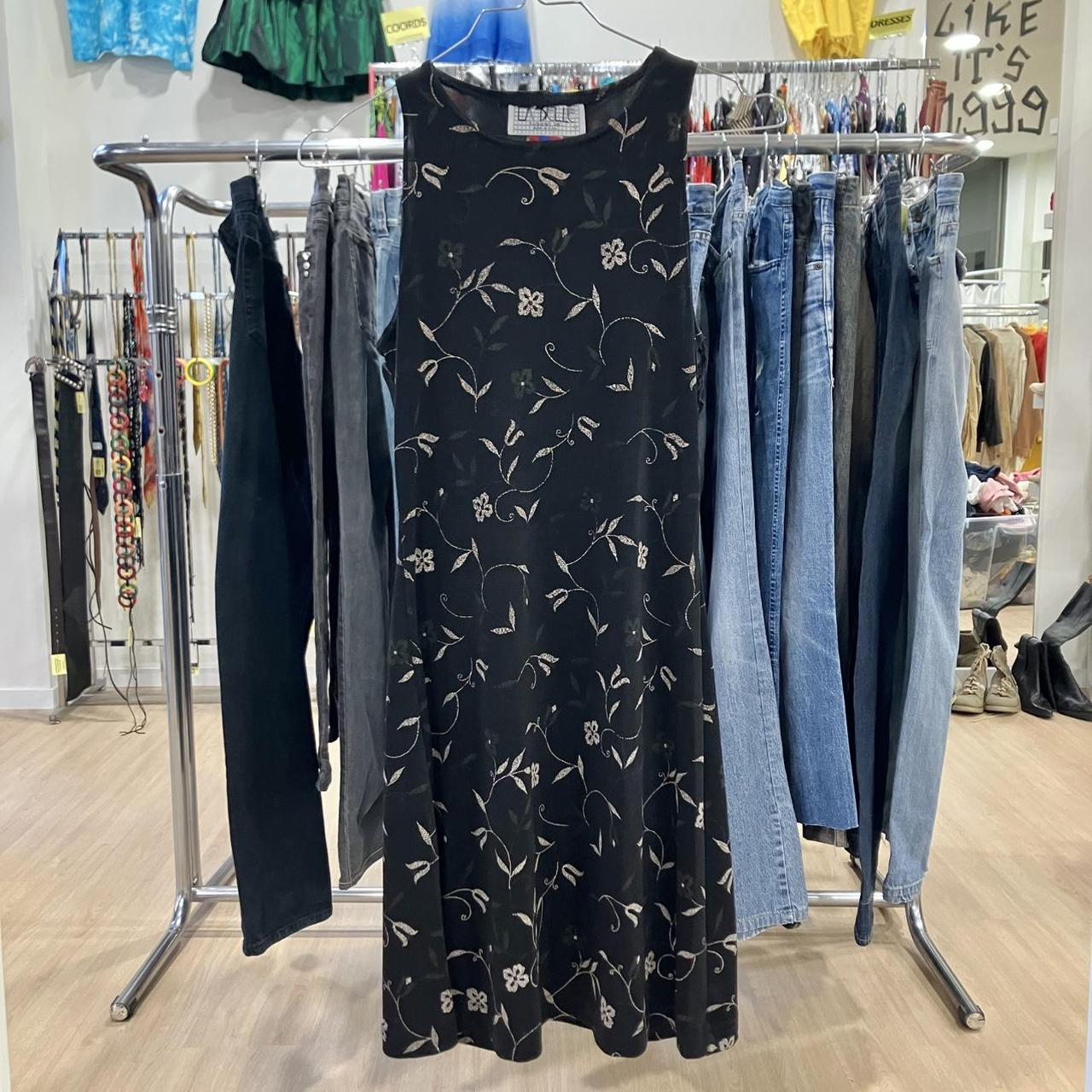 Black floral dress hanging on a rack with jeans and other clothing in a store setting