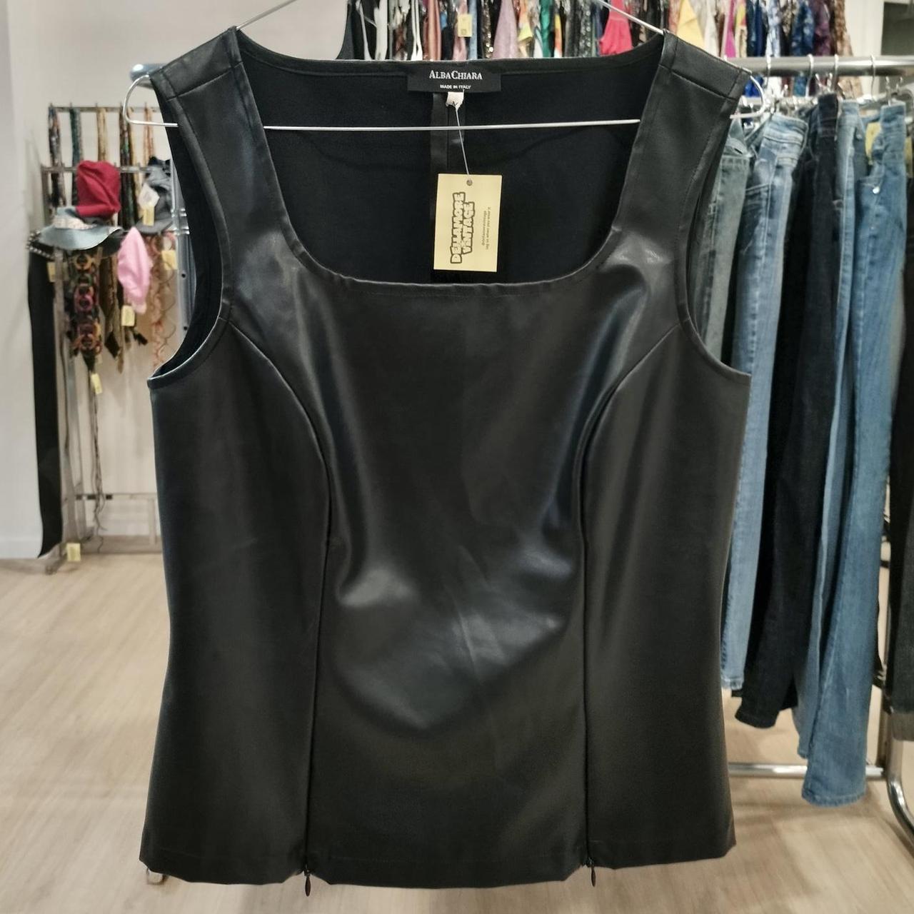 Black leather tank top on a rack with clothing in the background