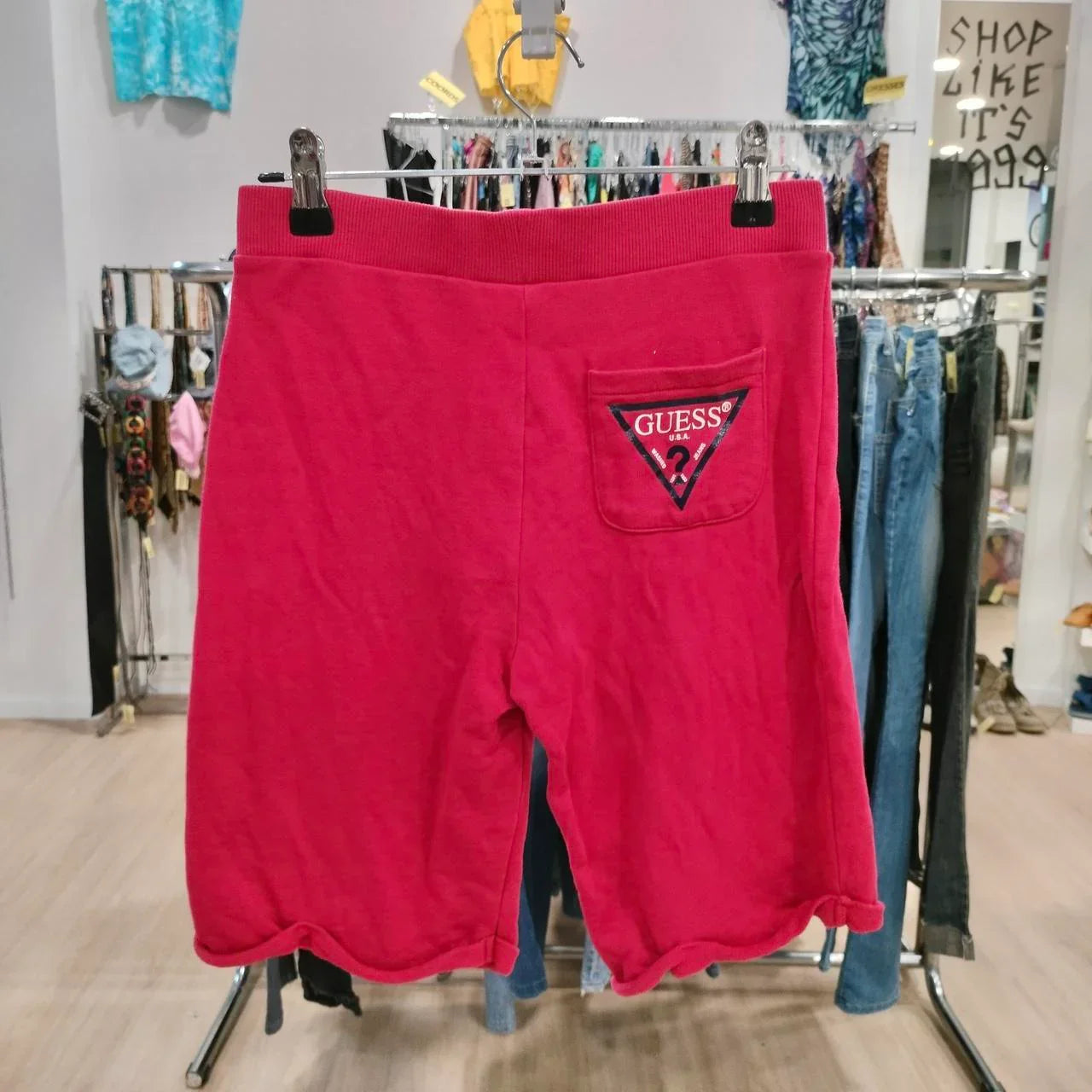 Red Guess shorts with logo patch on back pocket, displayed in a second hand fashion store
