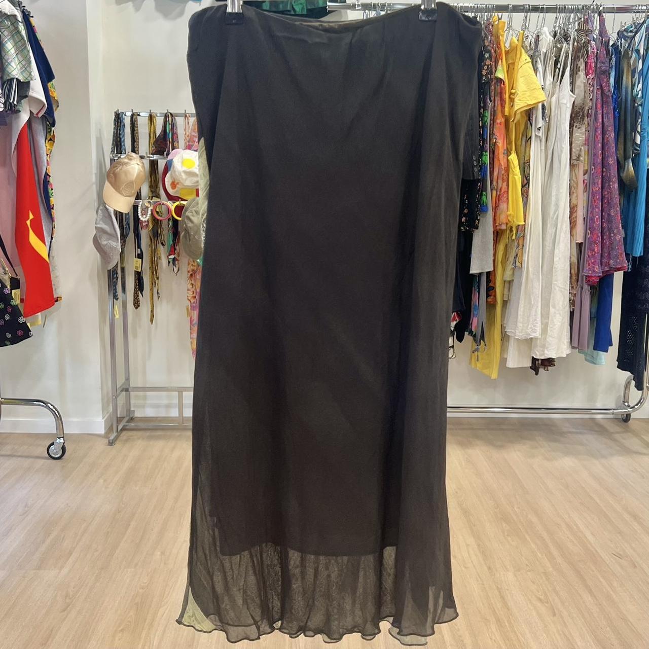 Sheer black maxi skirt on display in a vintage clothing store with colorful garments behind.