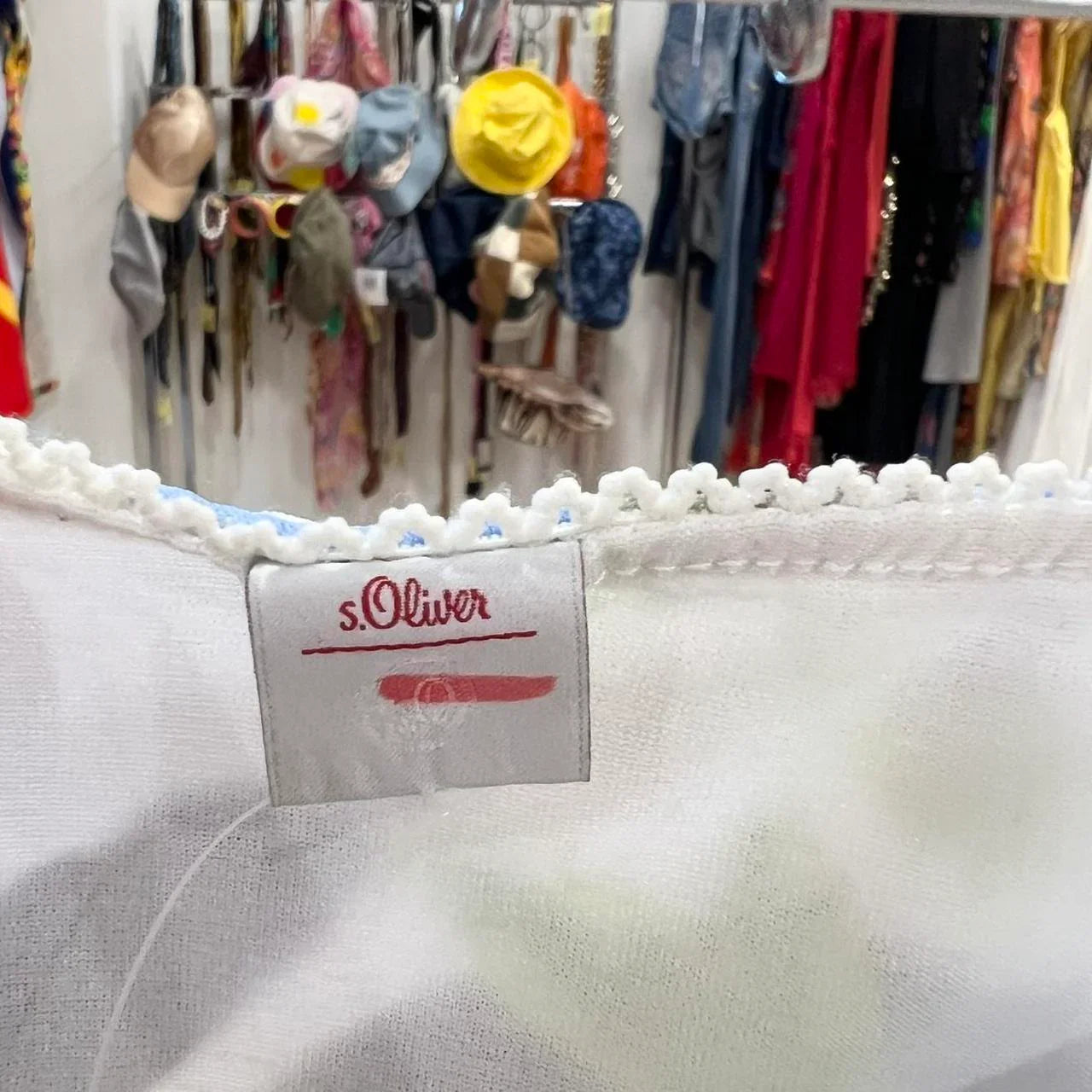 s.Oliver clothing label on white fabric with hats and clothing in second hand fashion store background