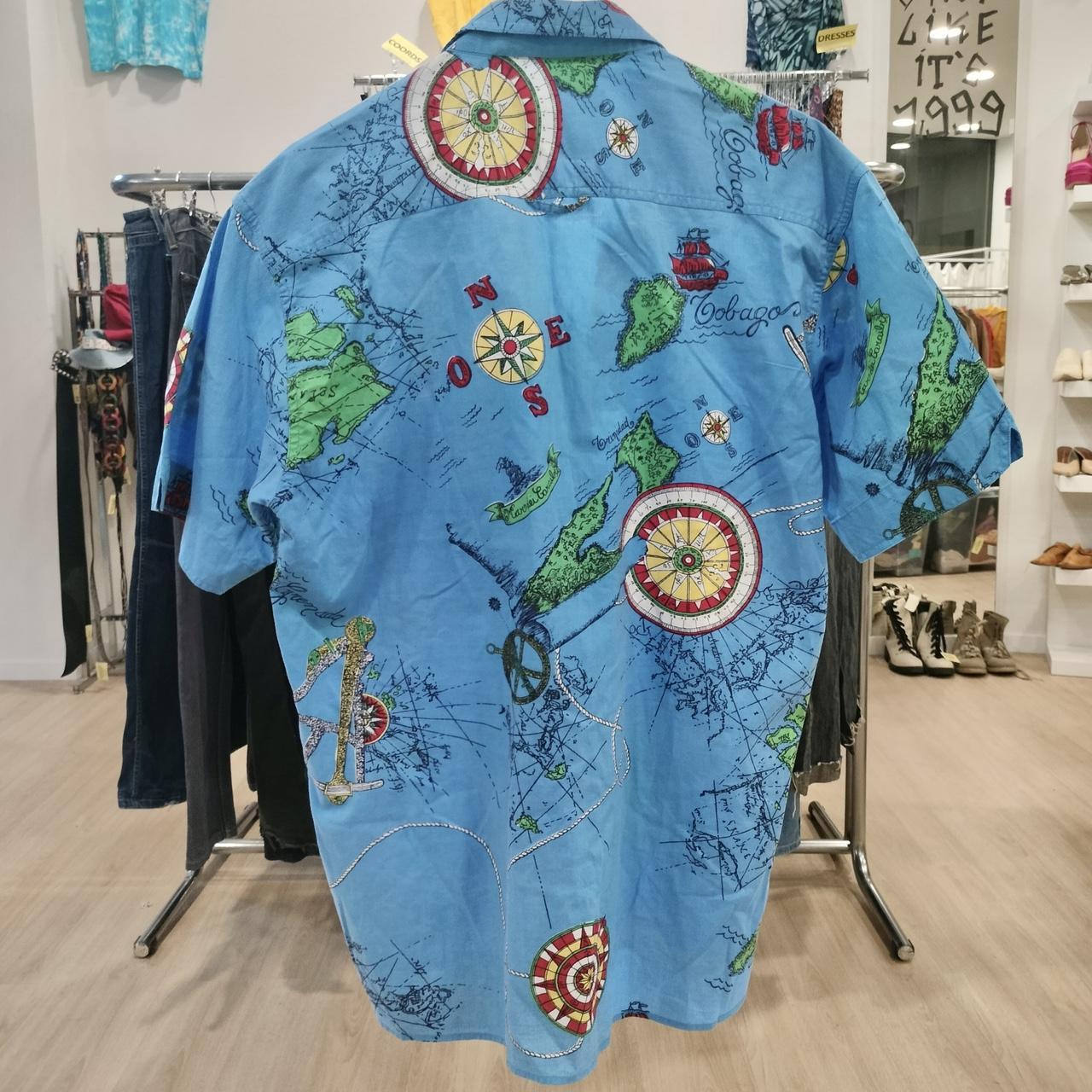 Blue short sleeve shirt with vintage map and compass print, hanging in thrift fashion store