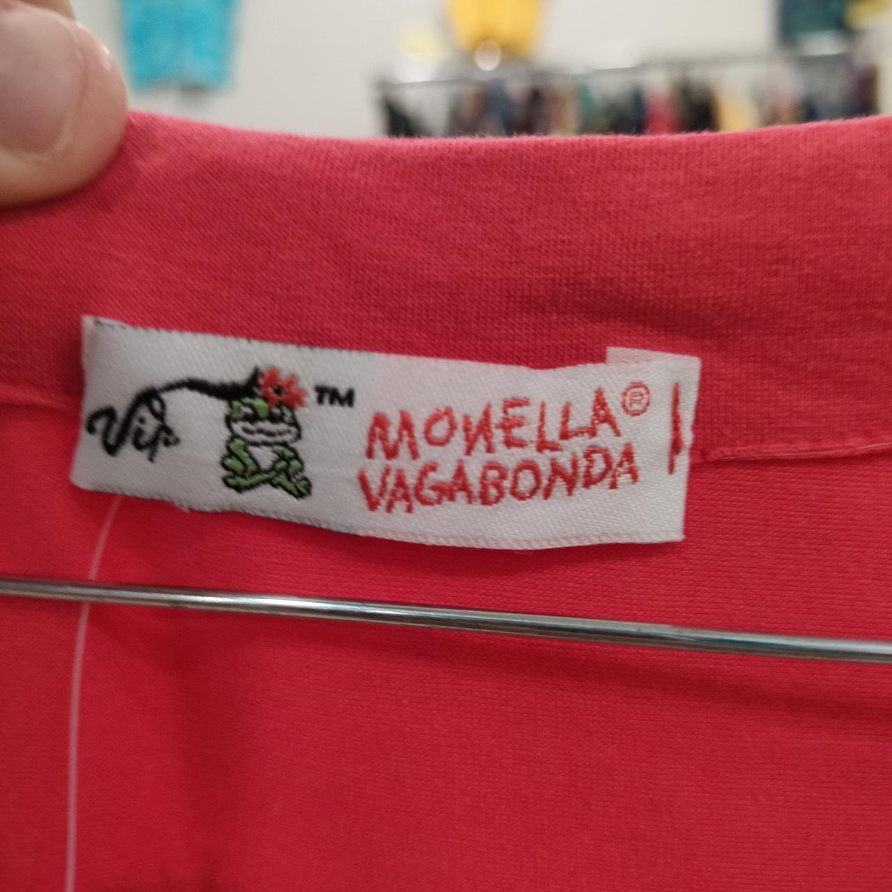 Close-up of a 'Monella Vagabonda' label on a red fabric background