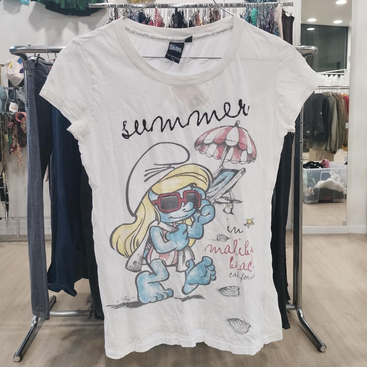 White graphic T-shirt with cartoon beach design and summer text, hanging in a clothing store