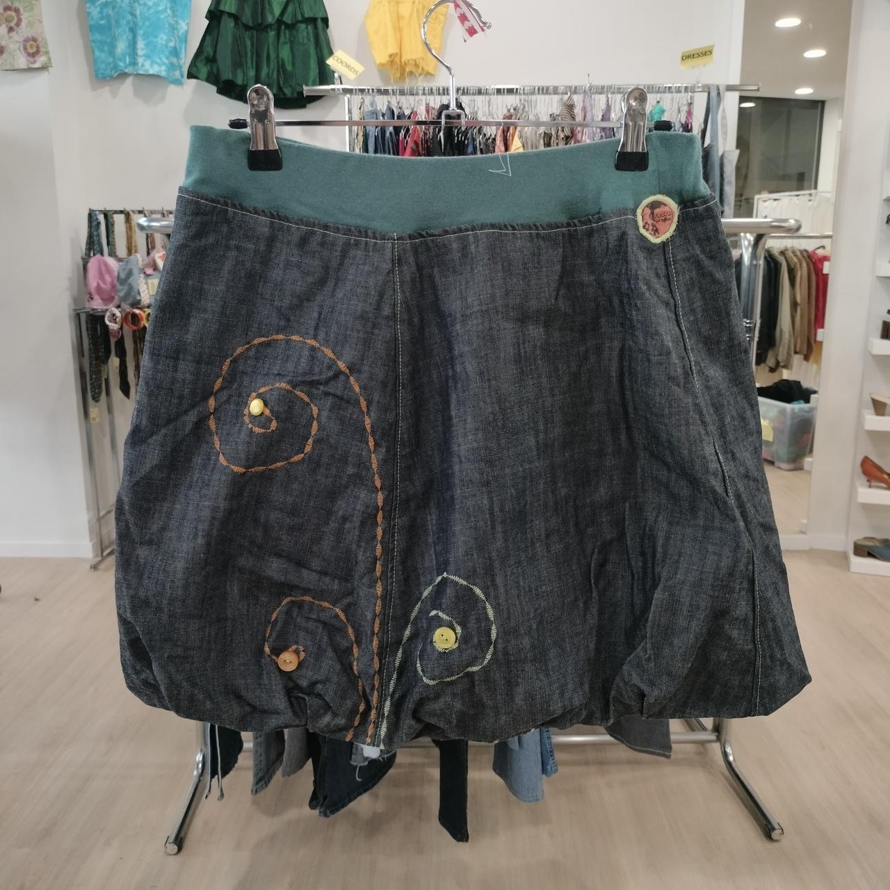 Dark denim A-line skirt with colorful embroidered swirl designs, displayed in a thrift fashion store
