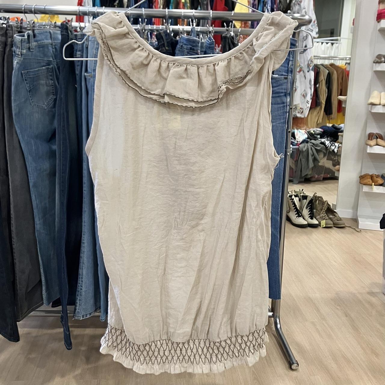 Beige sleeveless ruffle blouse with smocked hem, displayed in sustainable fashion store
