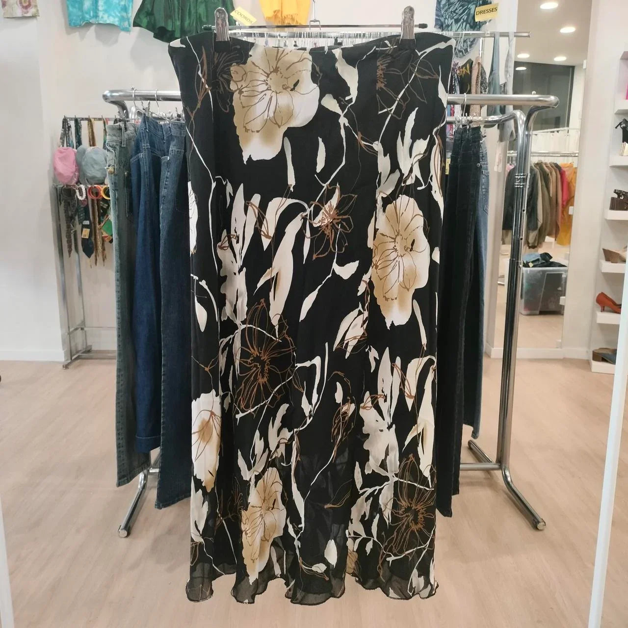 Black floral midi skirt with beige and white flowers, displayed in a second hand fashion store